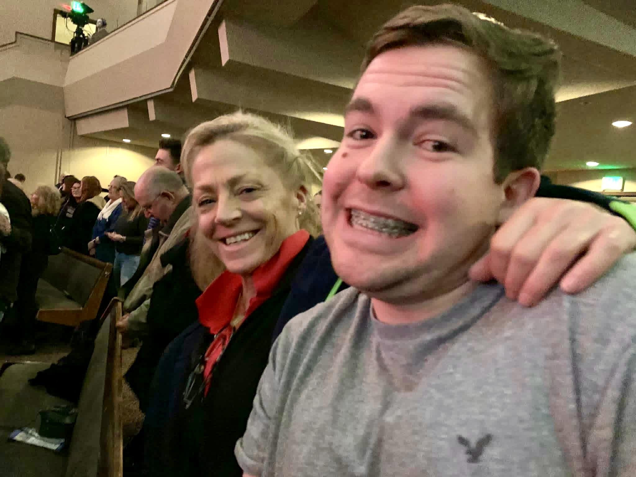 A man and a woman sit together at an event, both smiling and sharing a joyful moment.