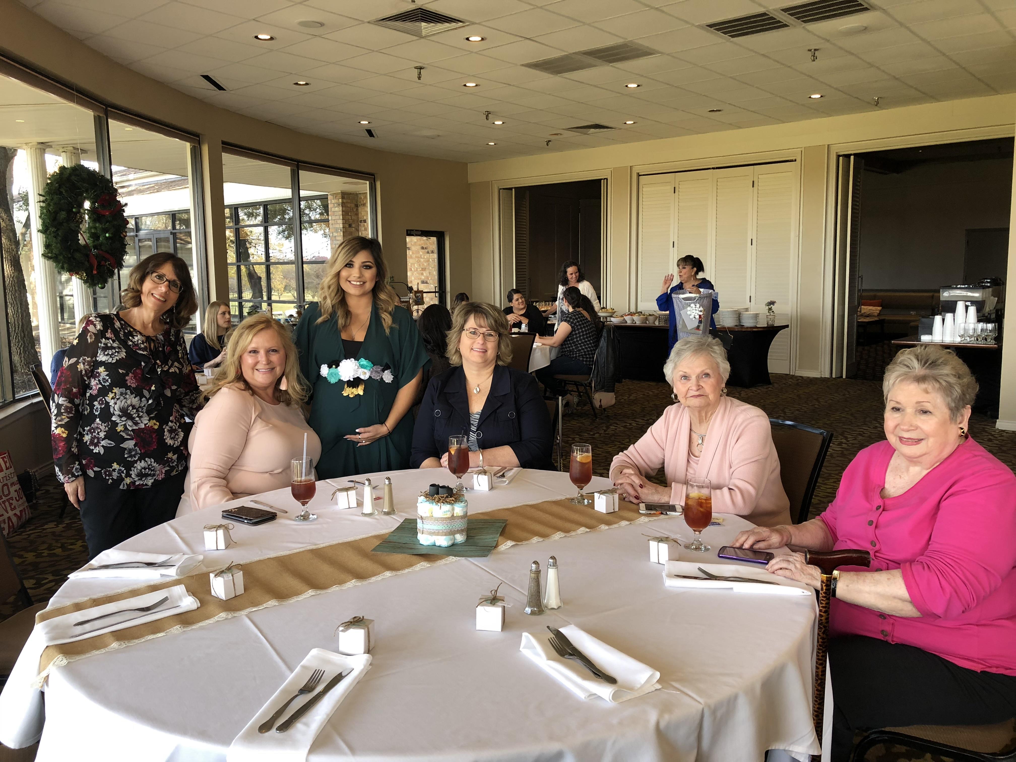 Group of women sit together at a round table enjoying lunch and drinks in a restaurant.