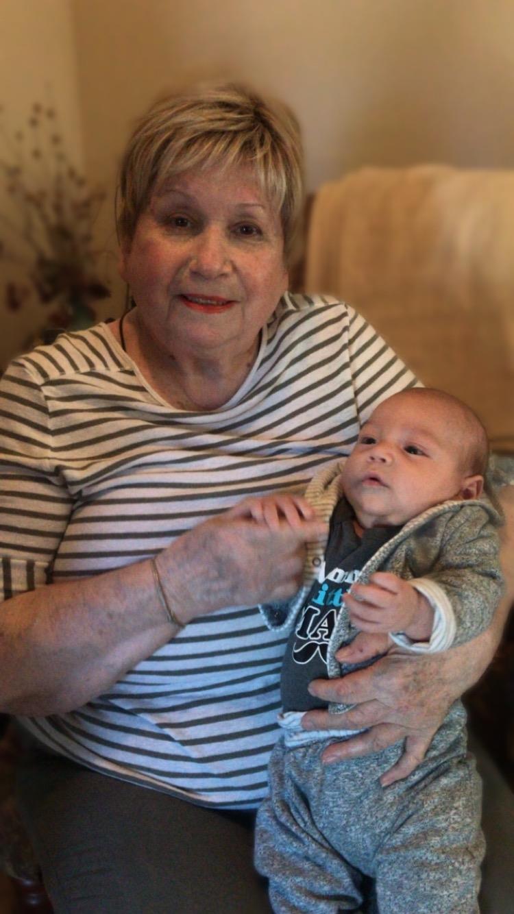 A grandmother sits inside holding her baby grandson in her arms during daytime.