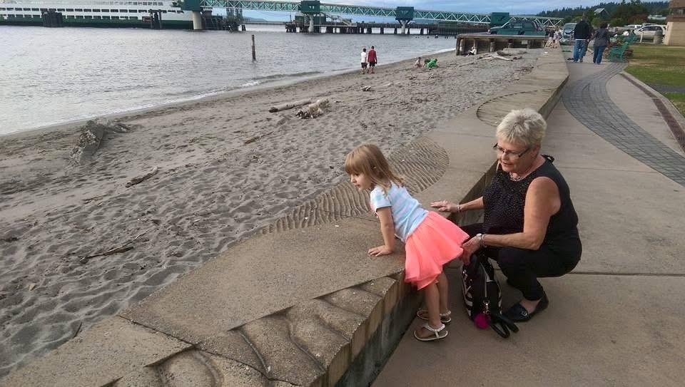 A child climbs on the wall while an adult watches closely. The water is in the background.