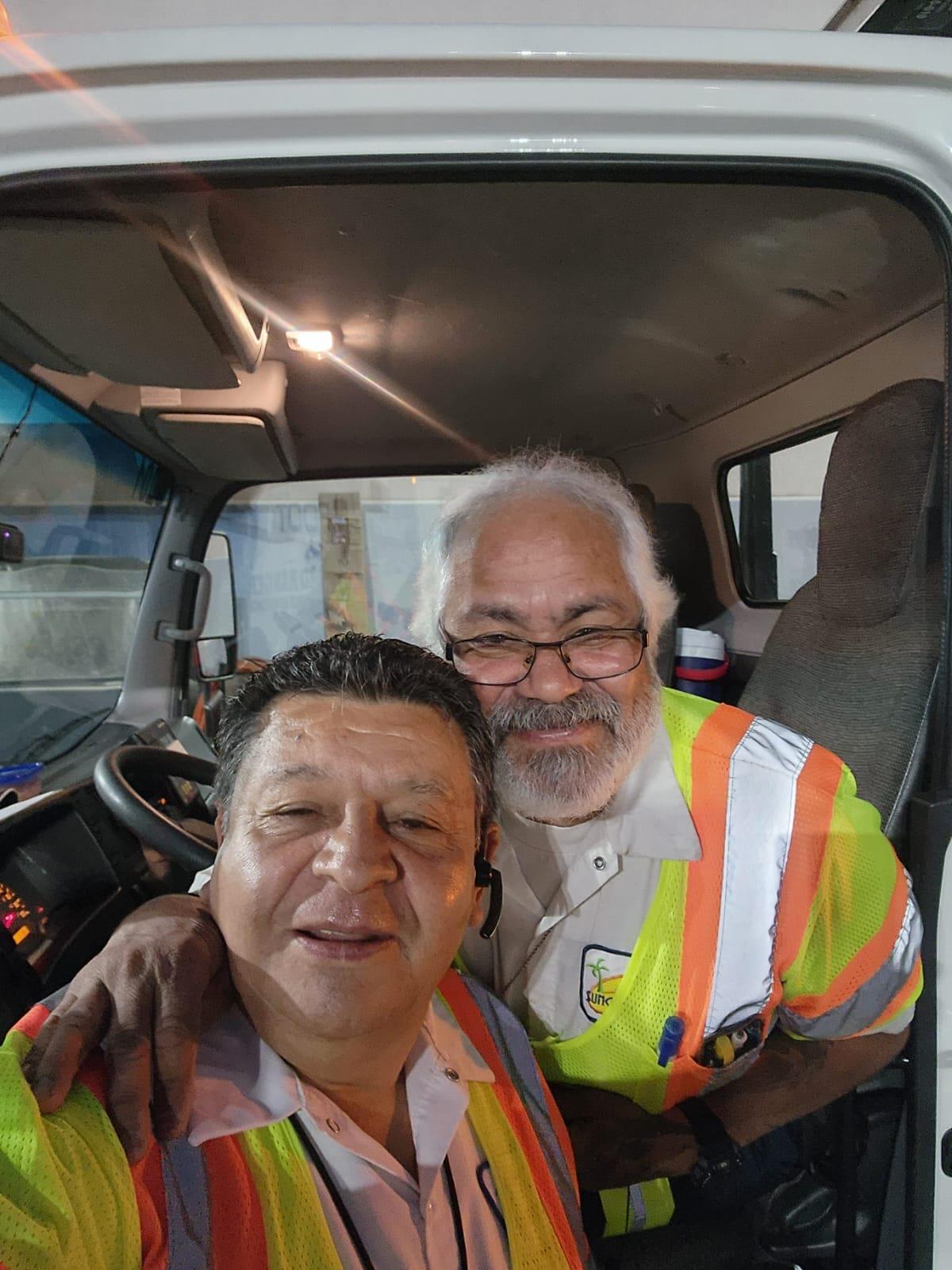 Two men smile as they take a selfie inside the truck during their work shift at a job site.