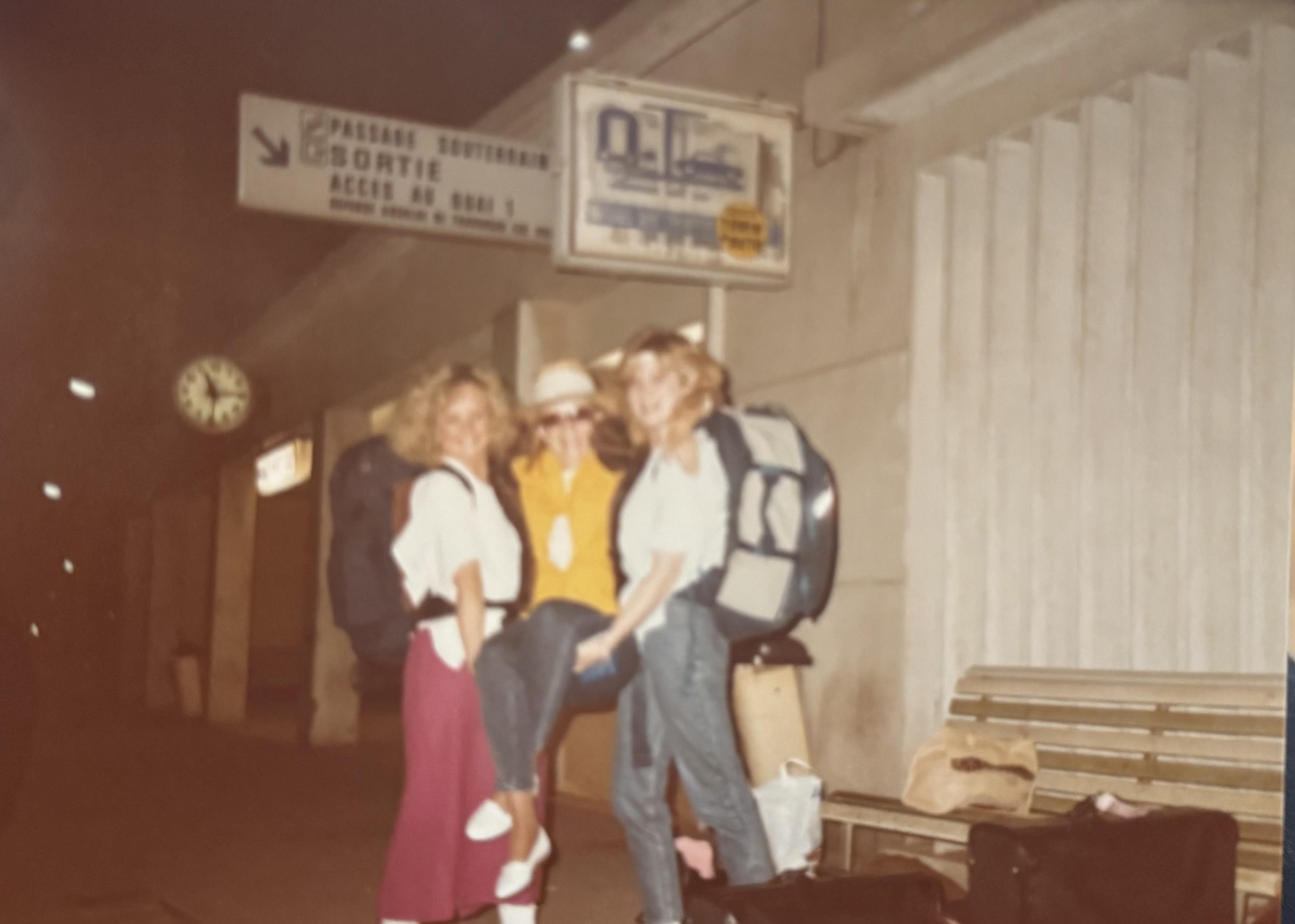 Friends are smiling and having fun outside a bus station at night with backpacks.