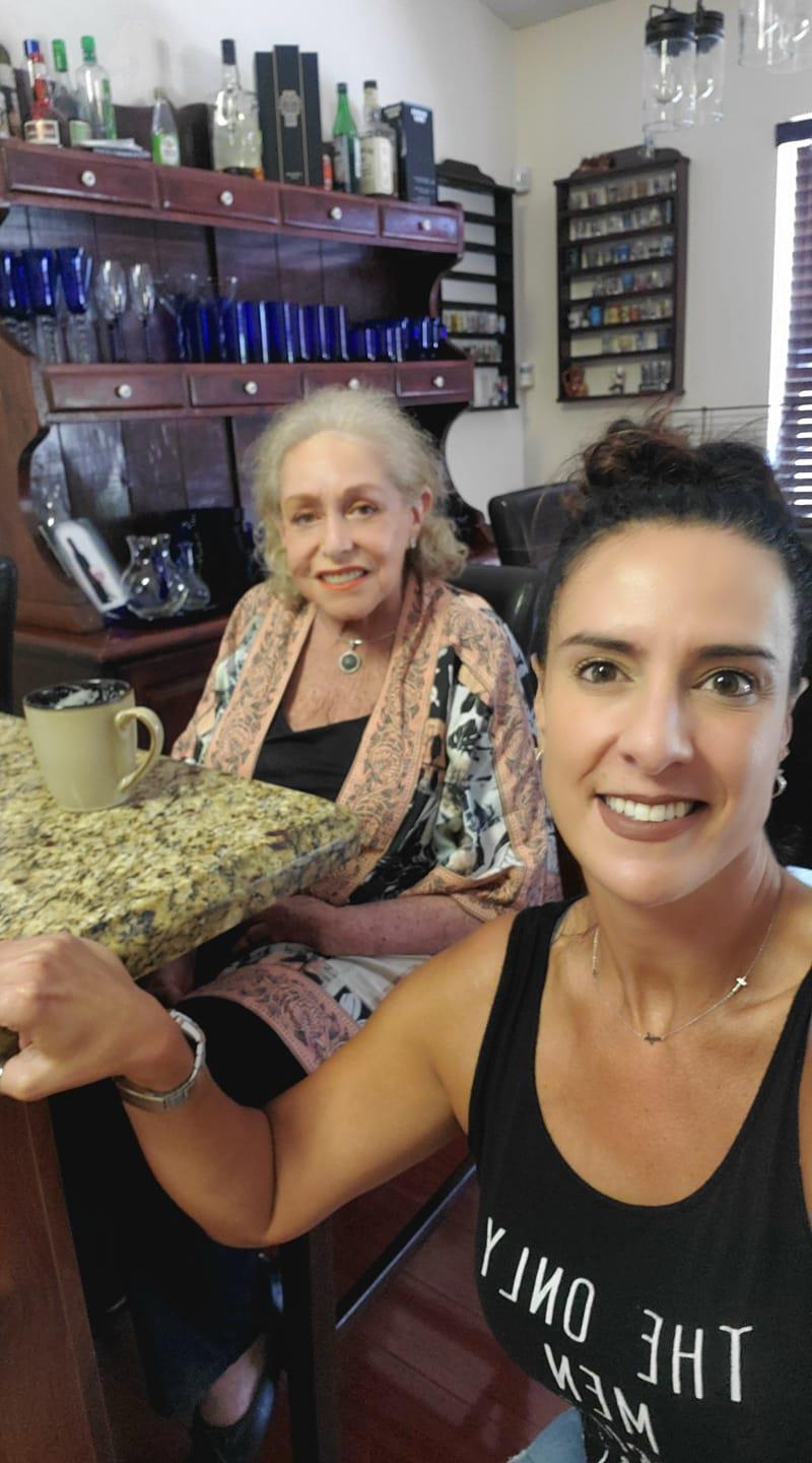 Two women enjoy a moment together at a table in a home. They share smiles and connection.