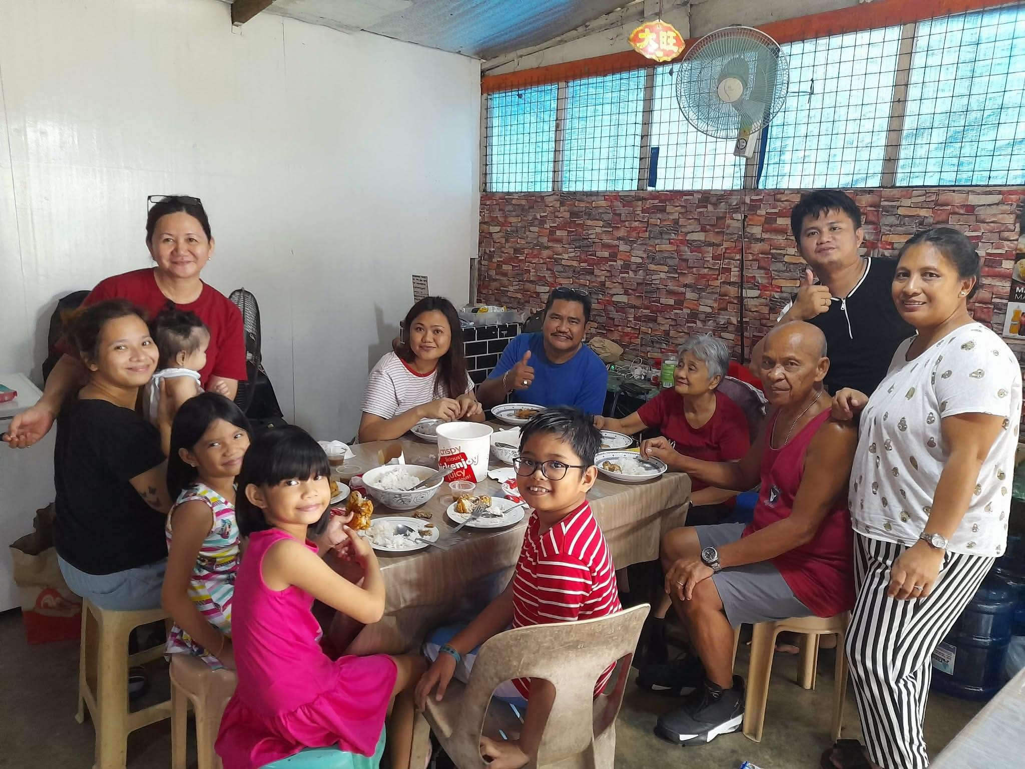 People gather around a table sharing food and conversation in a simple dining area.
