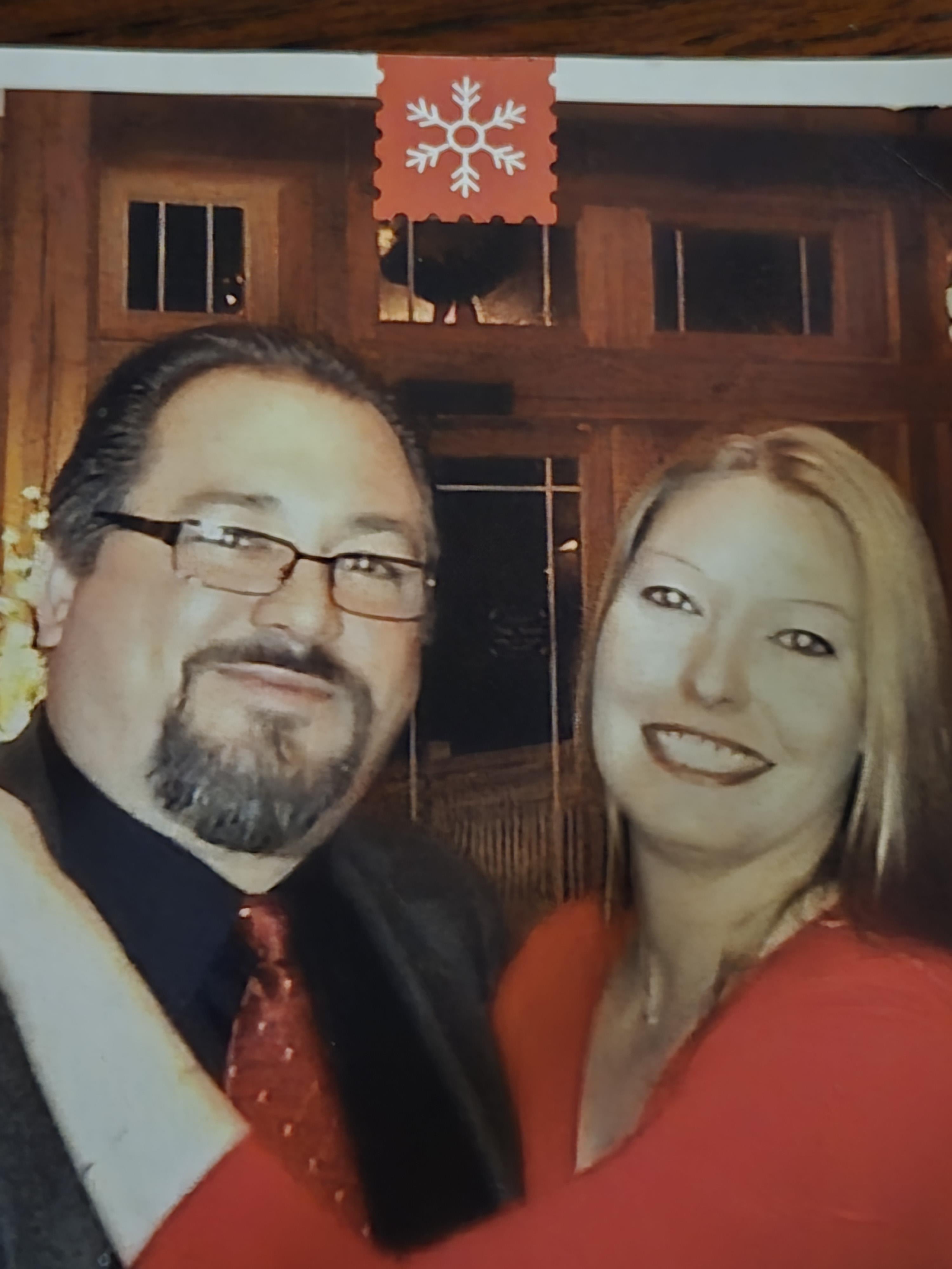 Couple stands close at a holiday gathering in a wooden venue with lights and decorations.