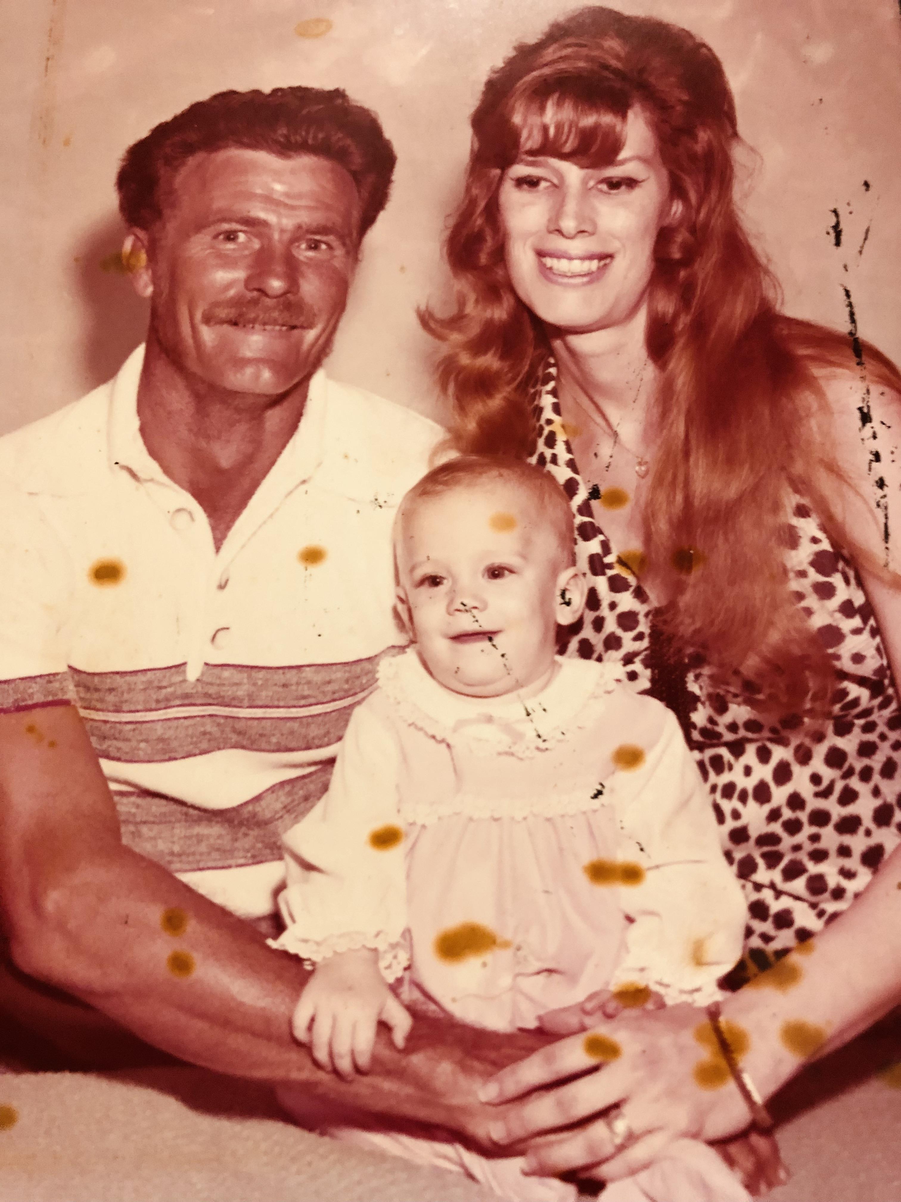 A man and woman sit together with a baby on their lap in a simple home.