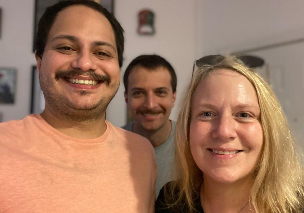 Three friends take a picture together in a room during a social event in the evening.
