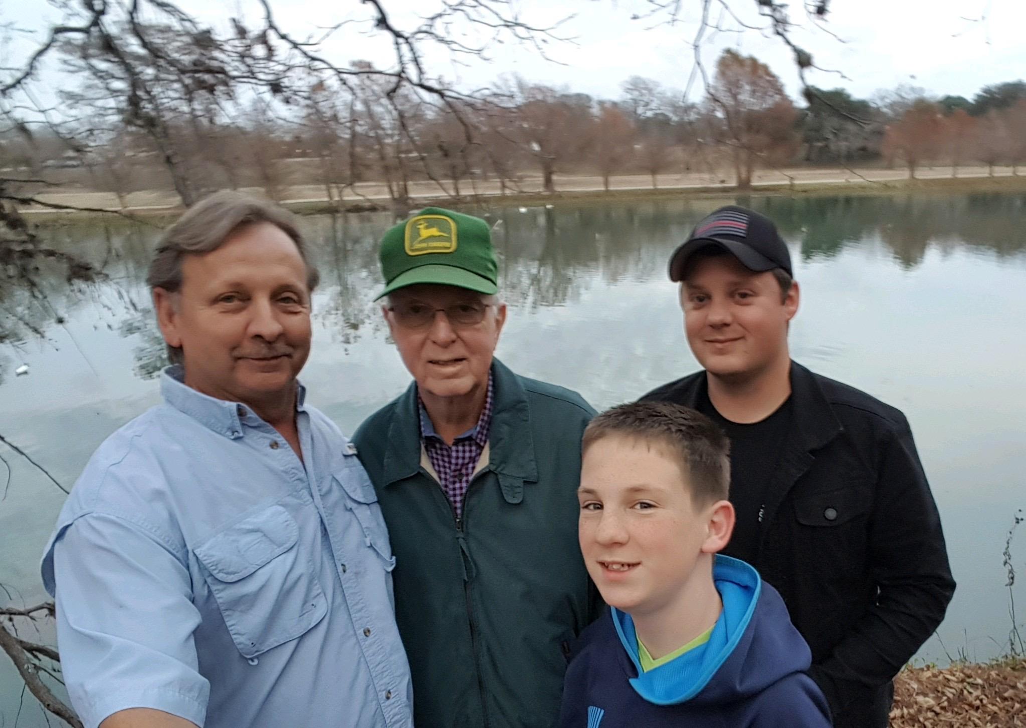 Four people stand together by a lake, sharing smiles while enjoying a nice day outdoors.