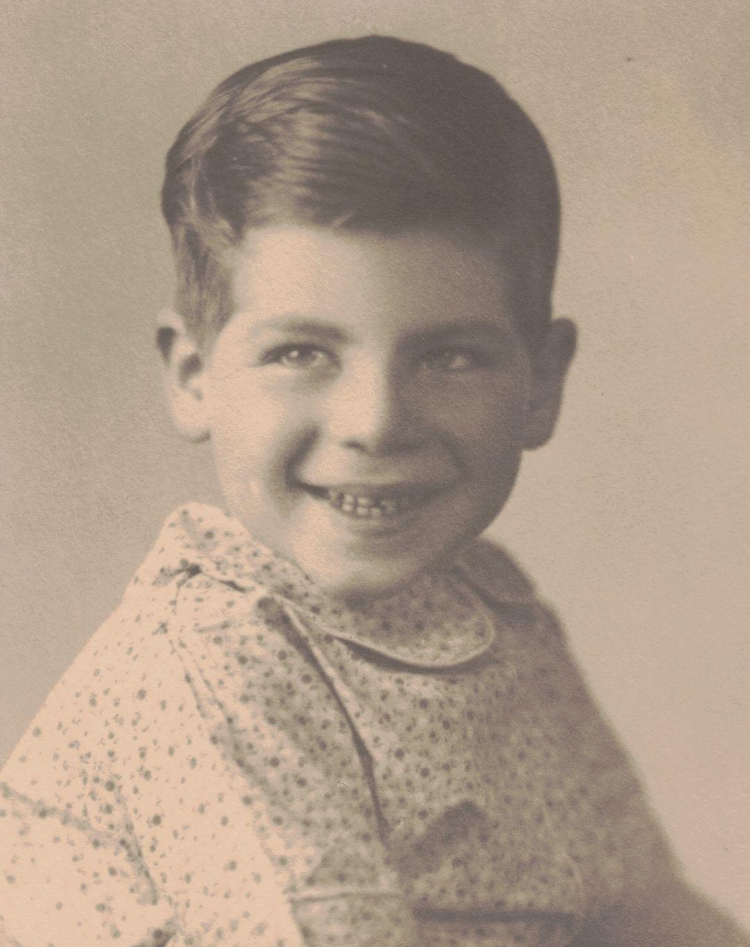 A young boy is looking at the camera with a smile, dressed in simple clothes and showing his teeth.