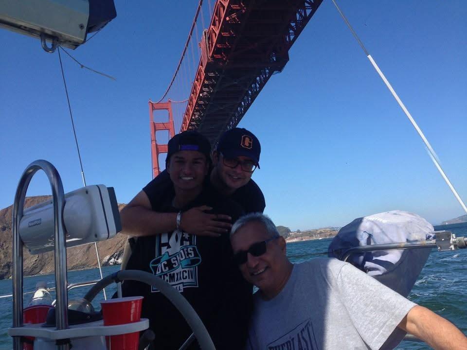 Three friends pose happily on a boat, with the Golden Gate Bridge in the background on a sunny day.