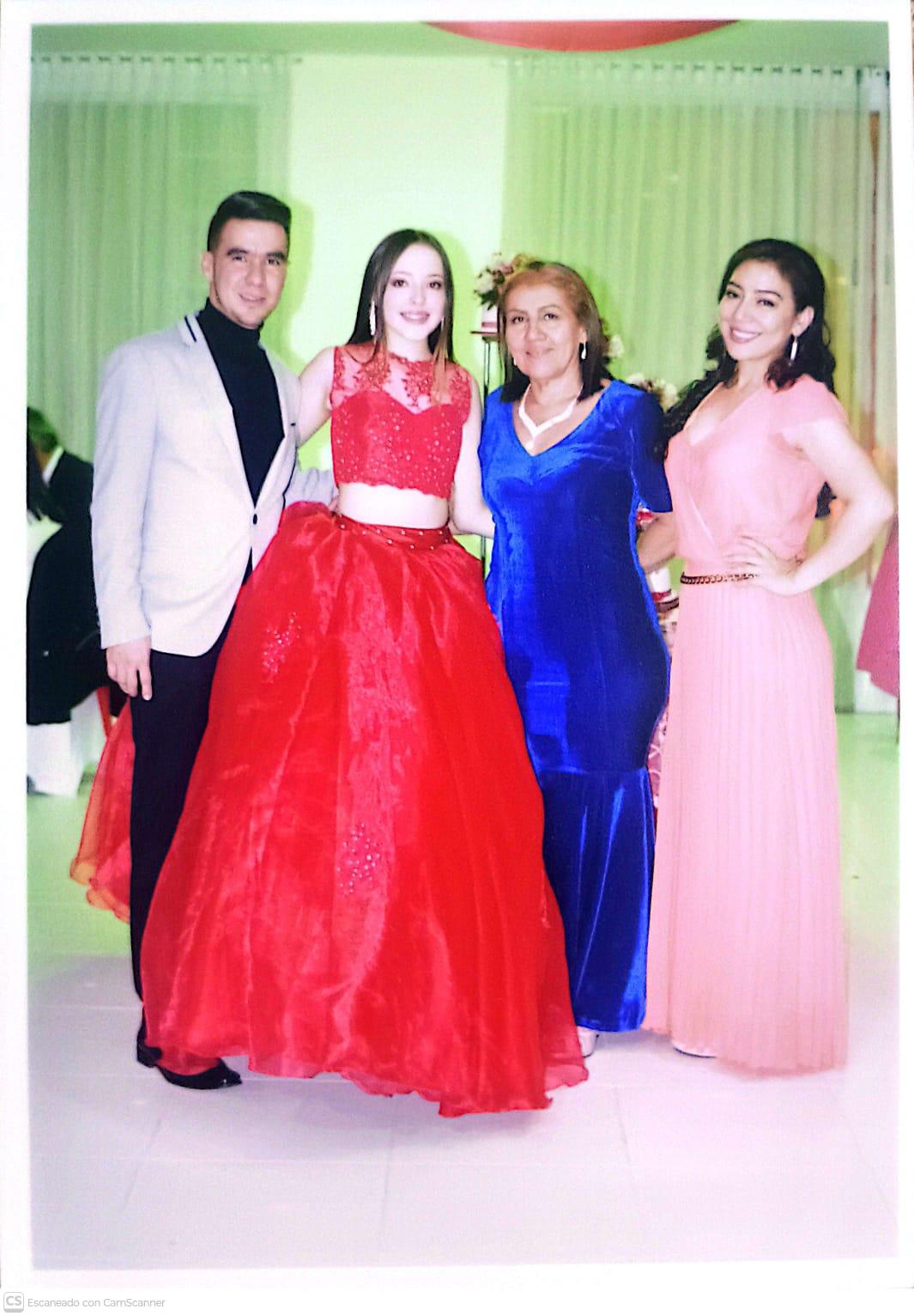 Four people stand close together, smiling and celebrating at a festive gathering in a hall.