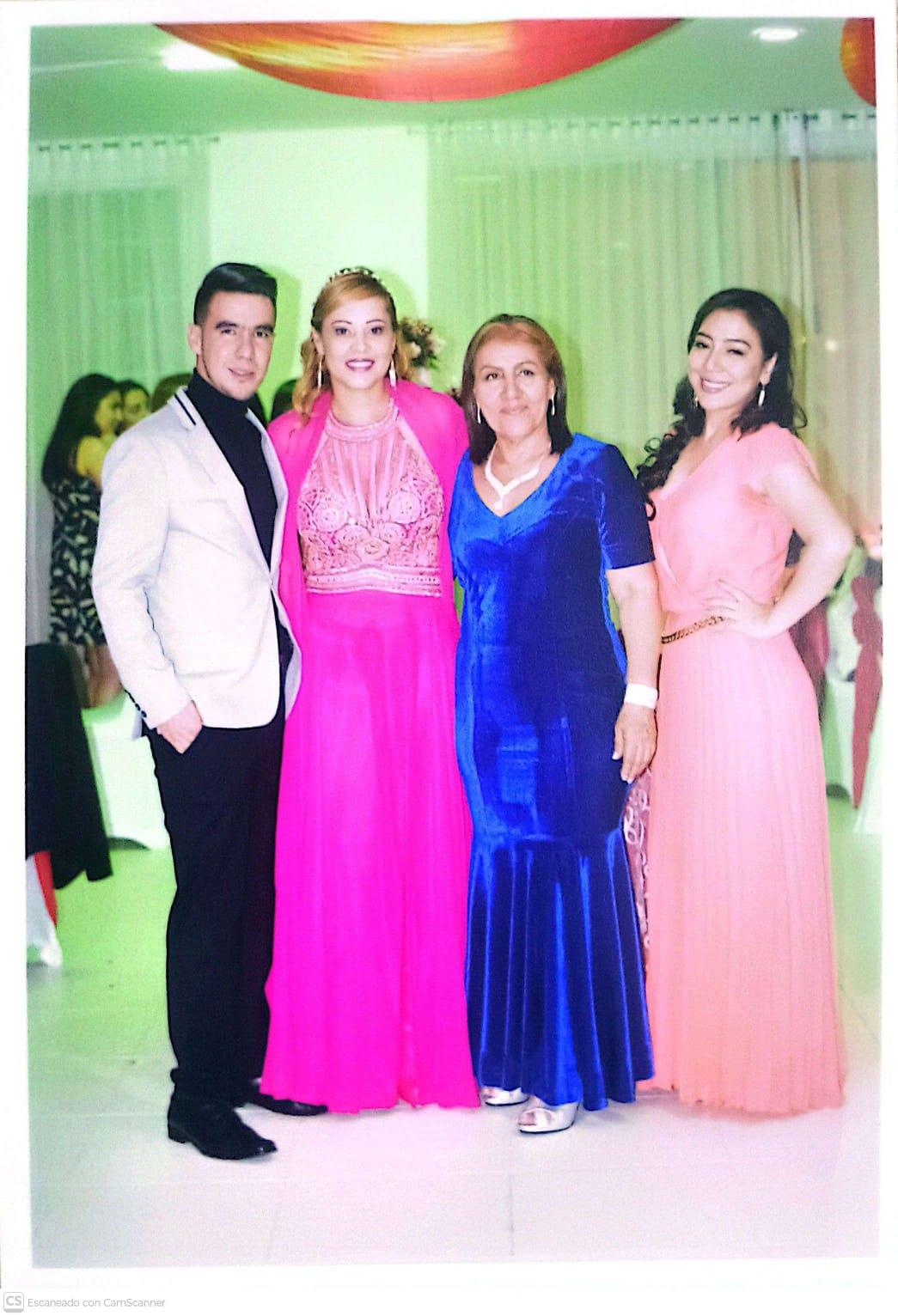 Four people smile together at a decorated venue with guests in the background.