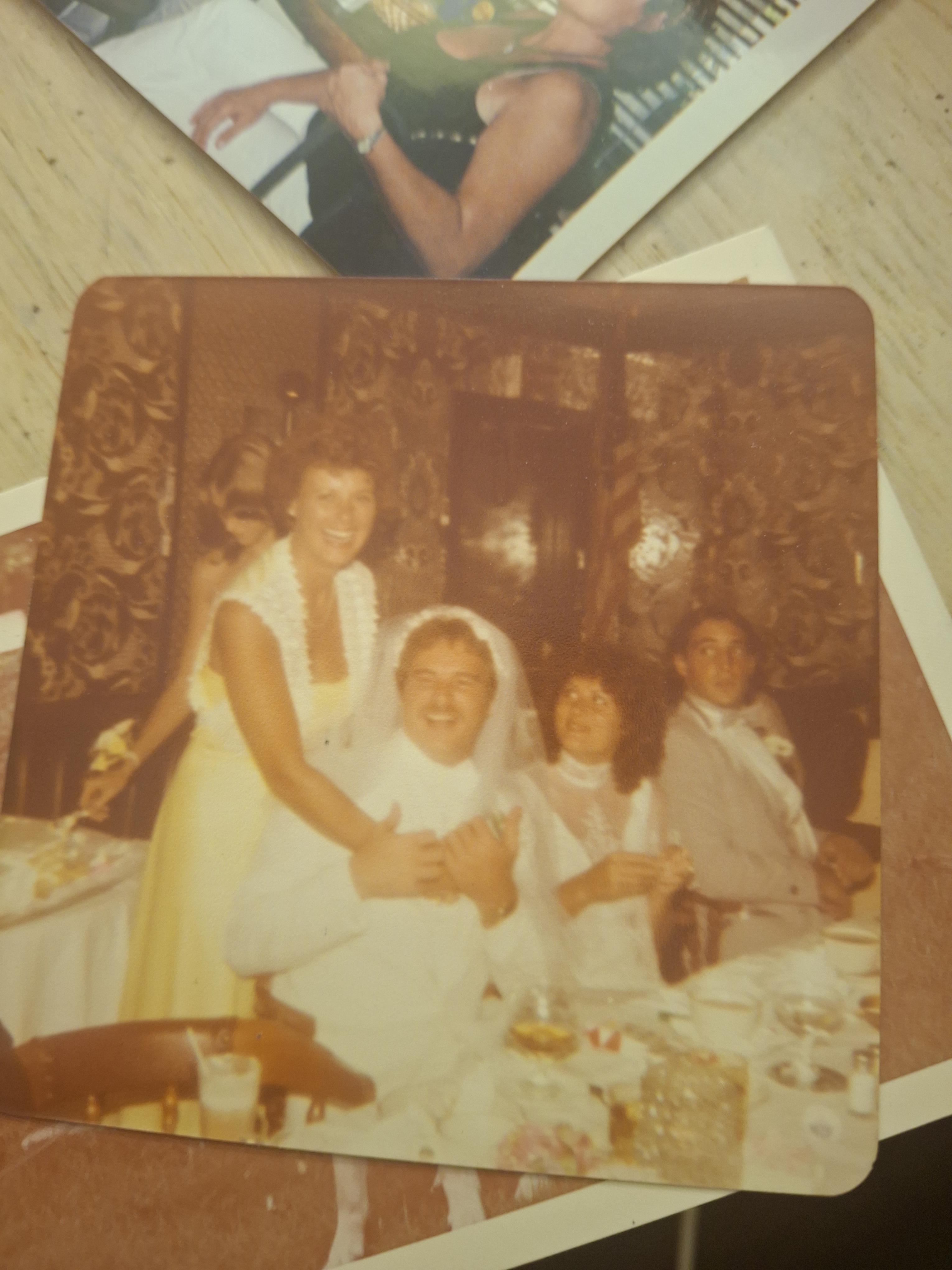 A group of children and adults gather around a table at a celebration with food and smiles.