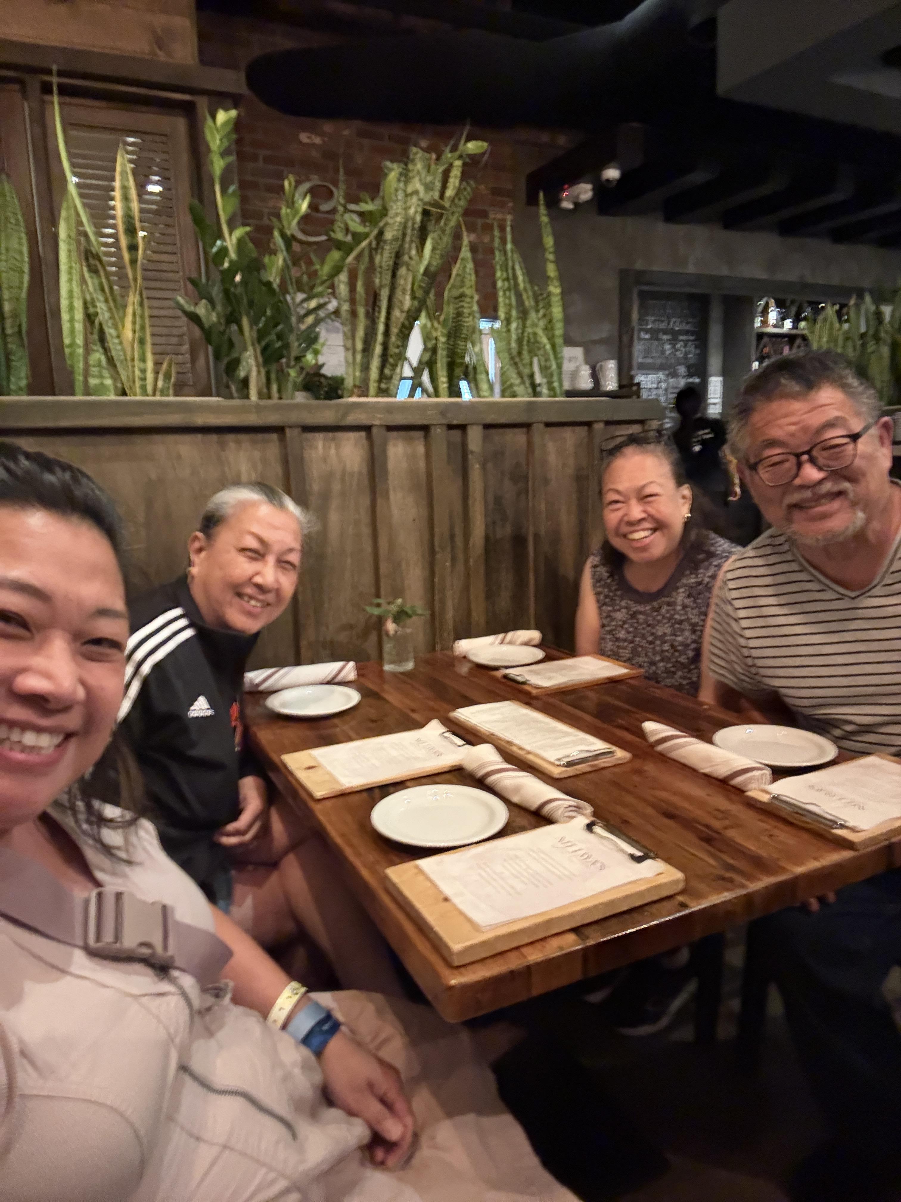 Four friends sit at a wooden table in a restaurant. They smile and enjoy their time together.