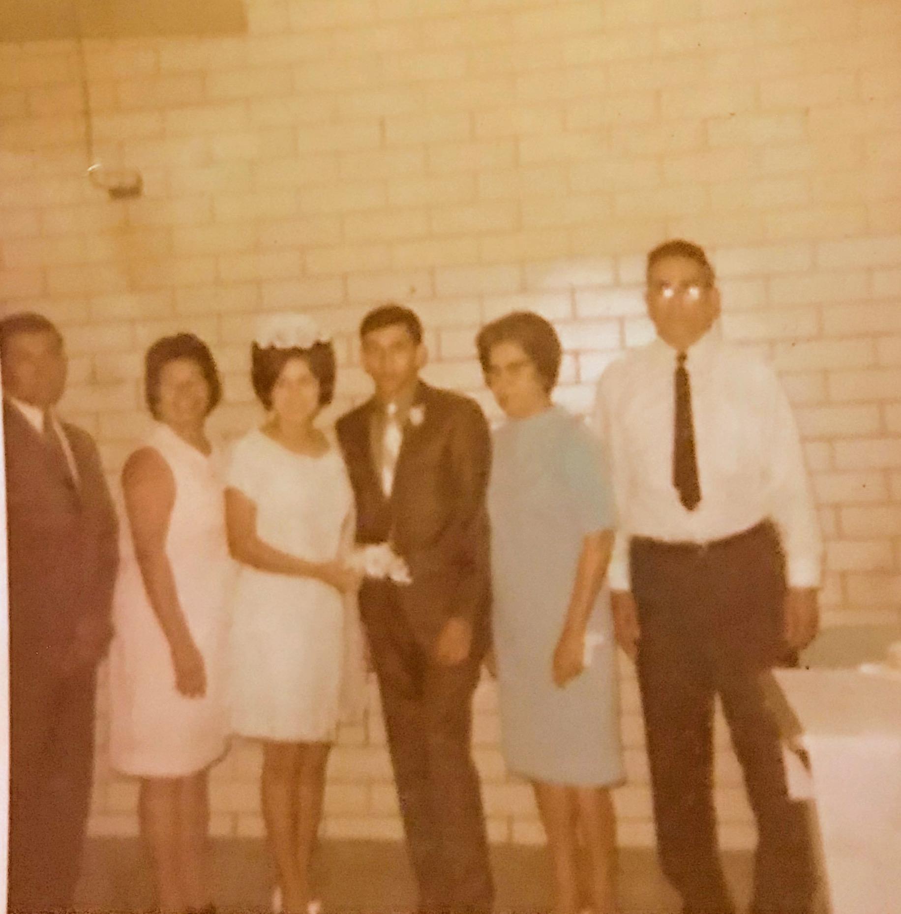 Six people stand together after a wedding ceremony, smiling and celebrating the occasion.