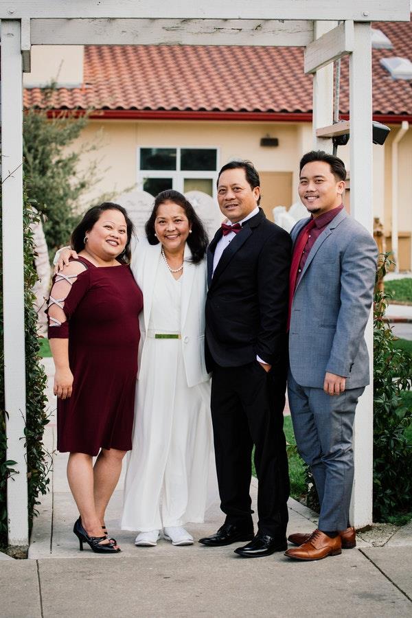 Four family members stand together outside a venue, smiling and dressed for a special event.