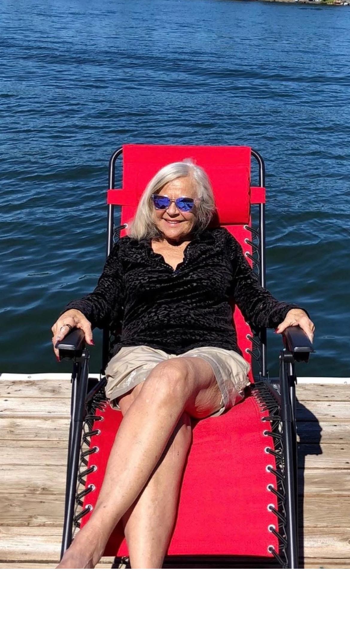 Woman sits comfortably on a chair by the water, enjoying a sunny day and relaxing in the moment.