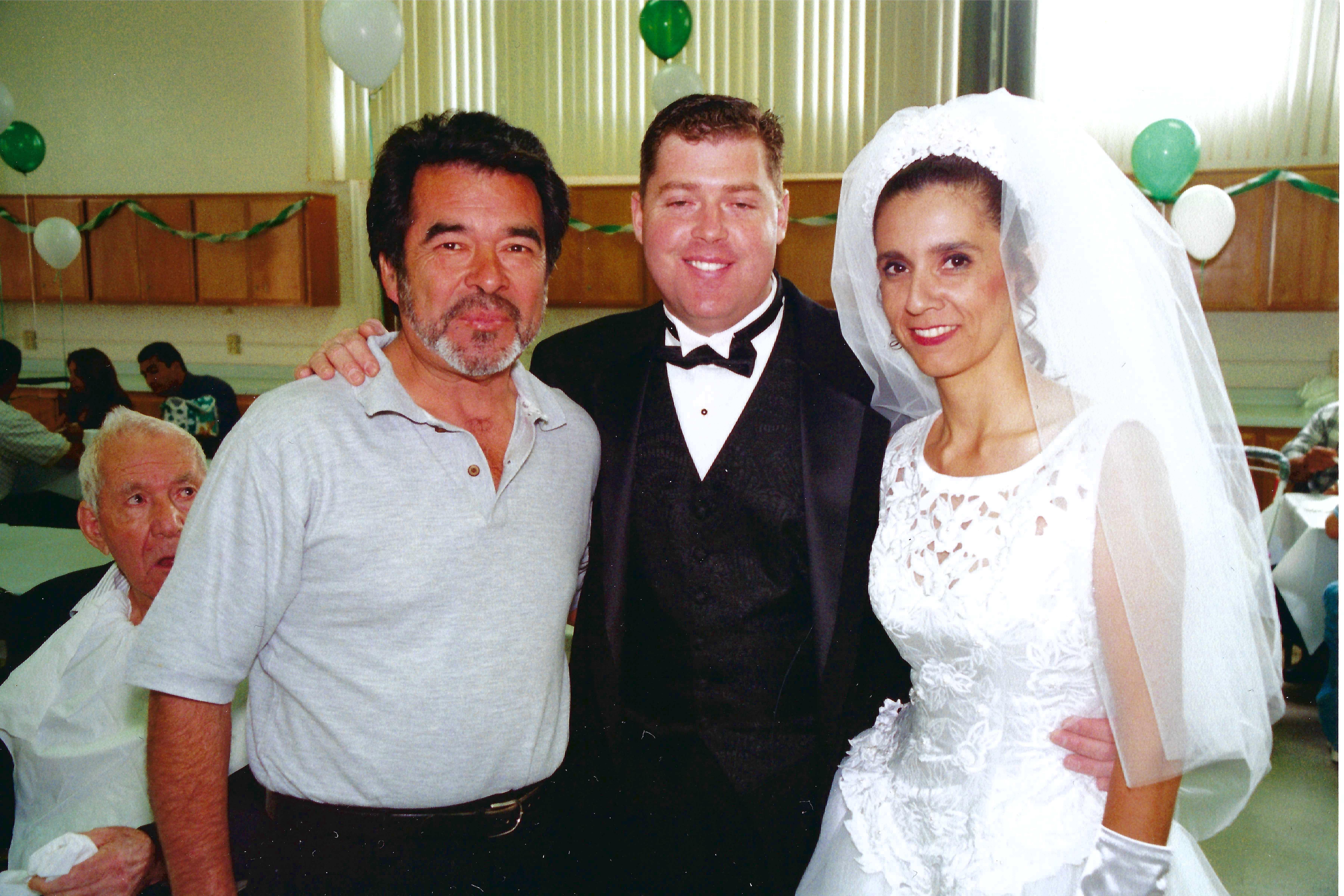 Three people stand together smiling at a wedding reception in a bright indoor space.
