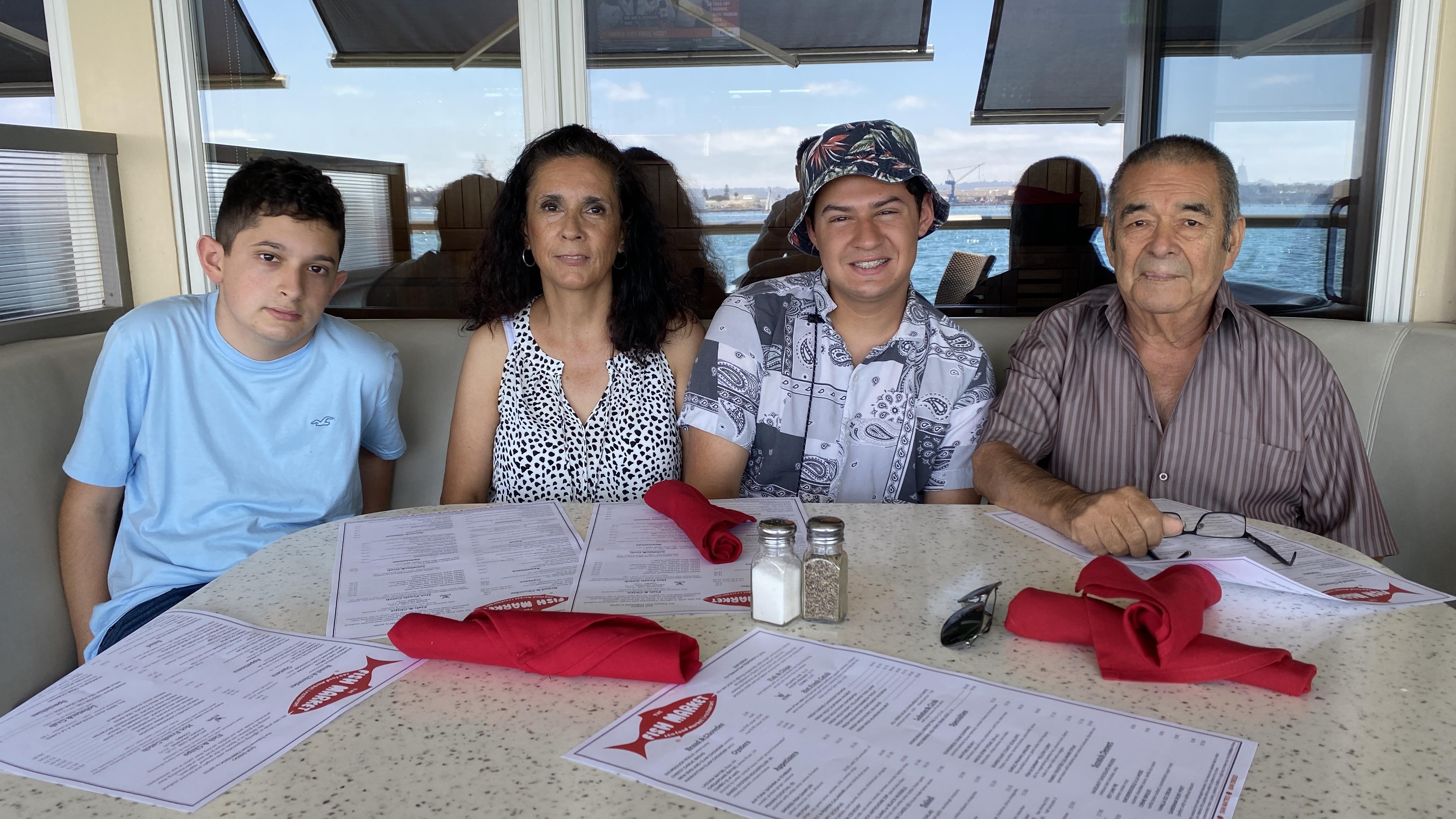 Four people sit at a table with menus, enjoying a meal and the view outside.