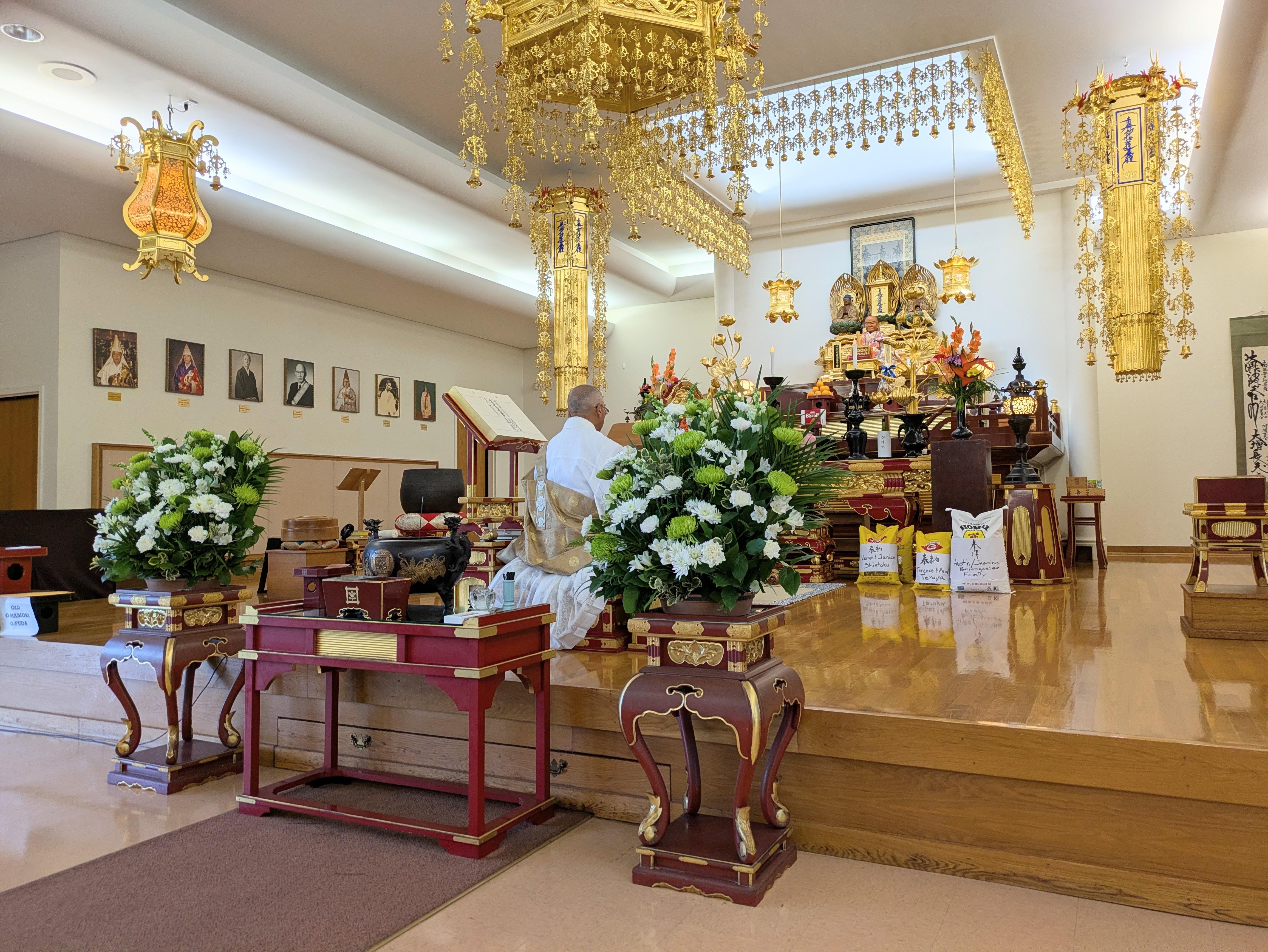 A monk practices a ritual in a temple decorated with flowers and golden items.