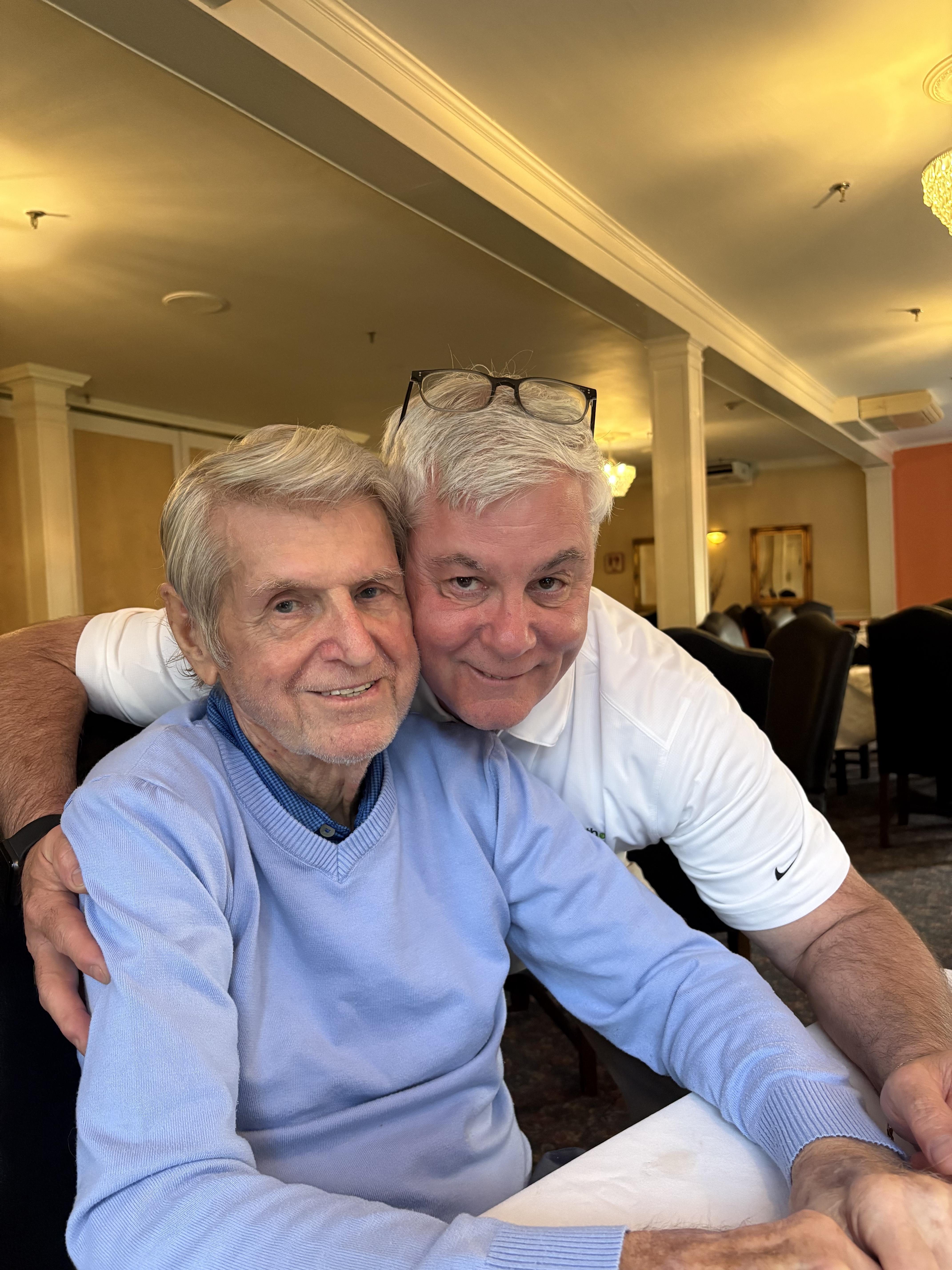Two men sit closely together, smiling and enjoying each other's company in a dining area.