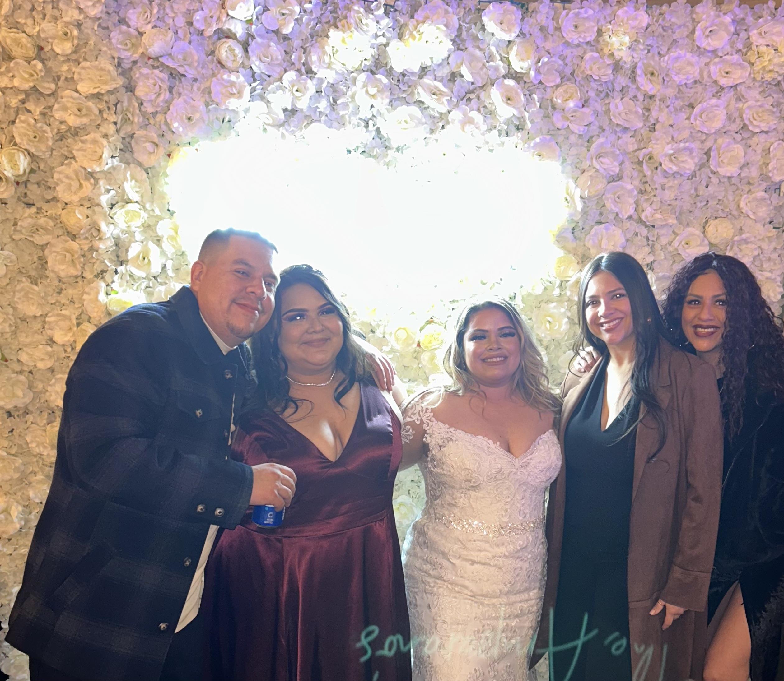 Friends stand together smiling at a wedding celebration with flowers in the background.