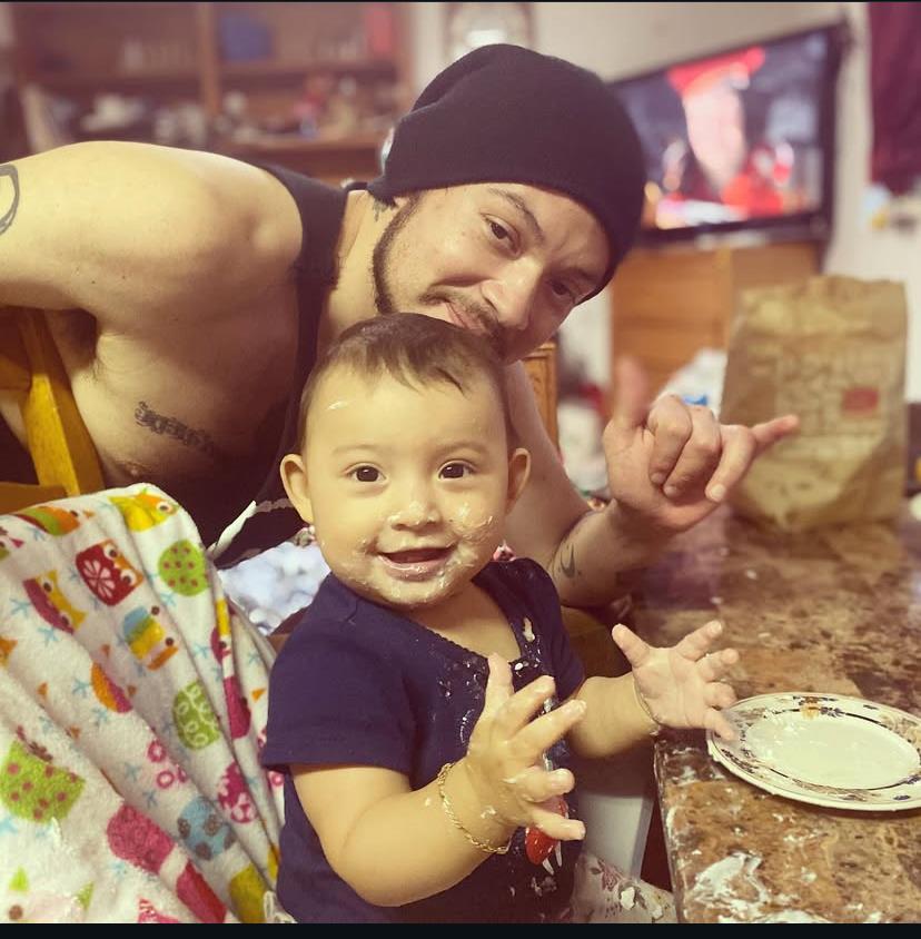 A man and his baby are having fun together in a kitchen. The child is smiling and playful.