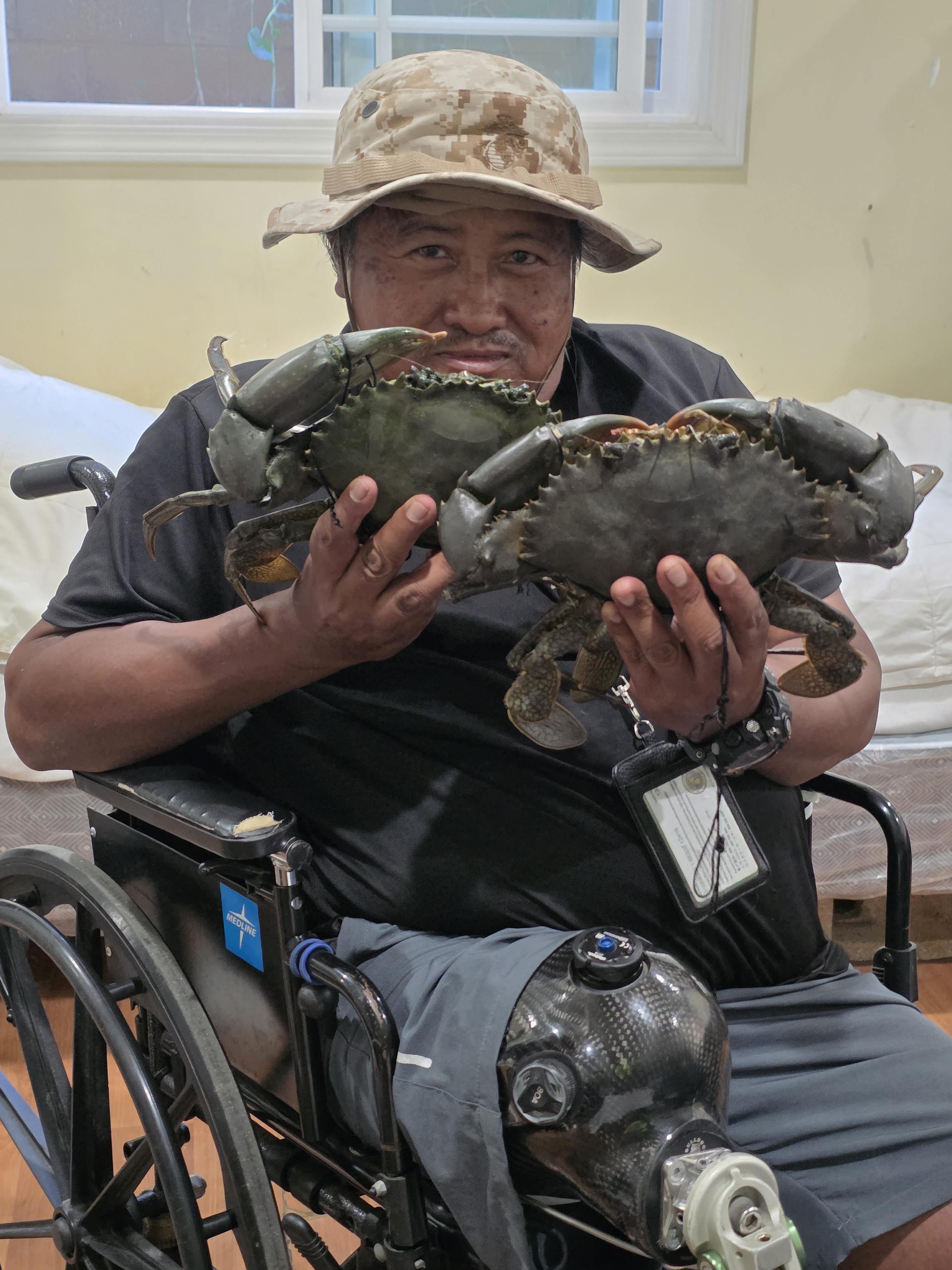 A man sits in a wheelchair and holds two crabs in his hands while inside a room.