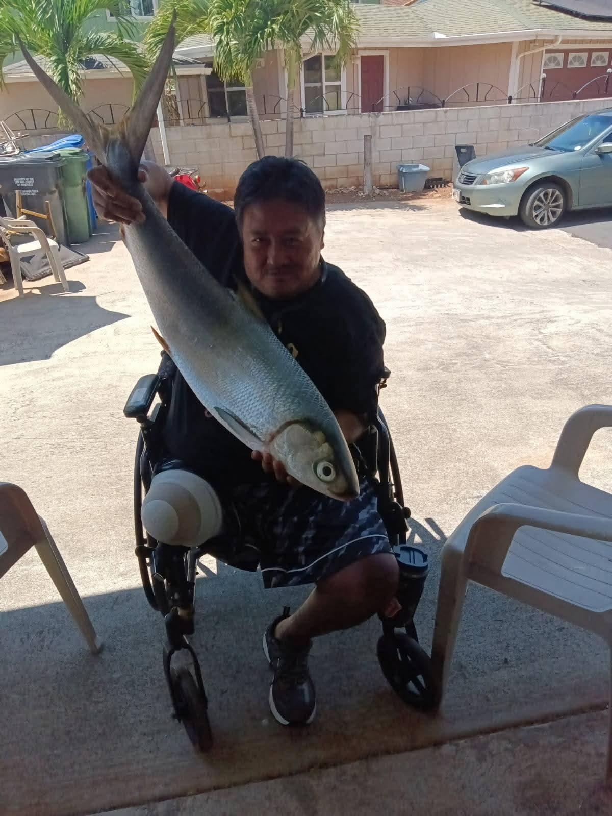 A man in a wheelchair catches a big fish while sitting outside near parked cars.