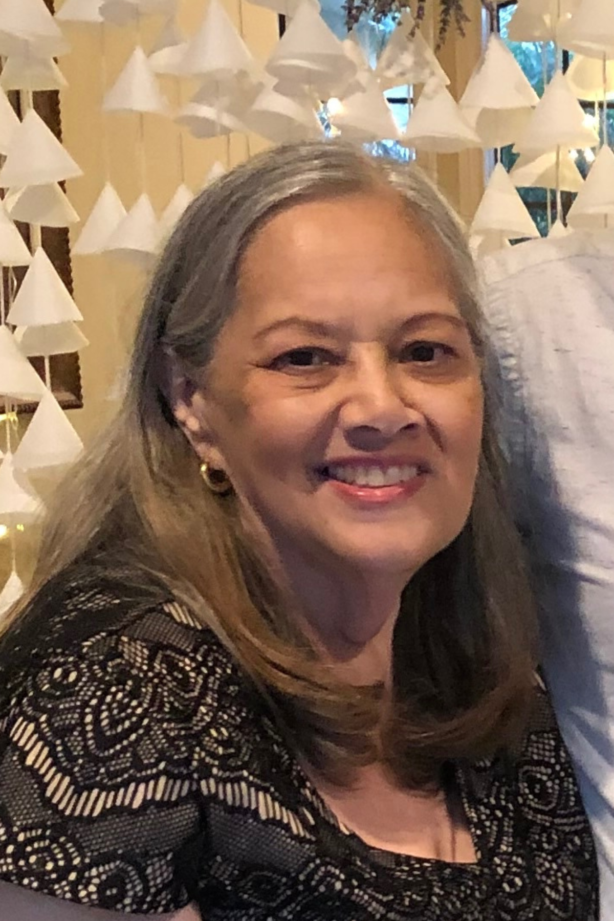 A woman sits with a smile, enjoying a gathering with friends and family in a decorated space.