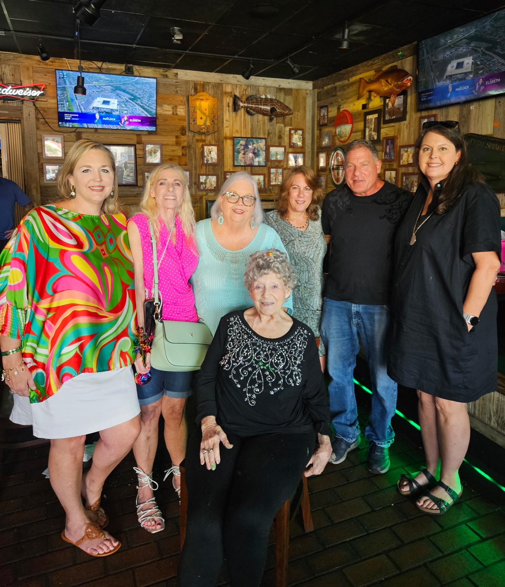 People stand and sit together smiling and enjoying their time at a local bar.