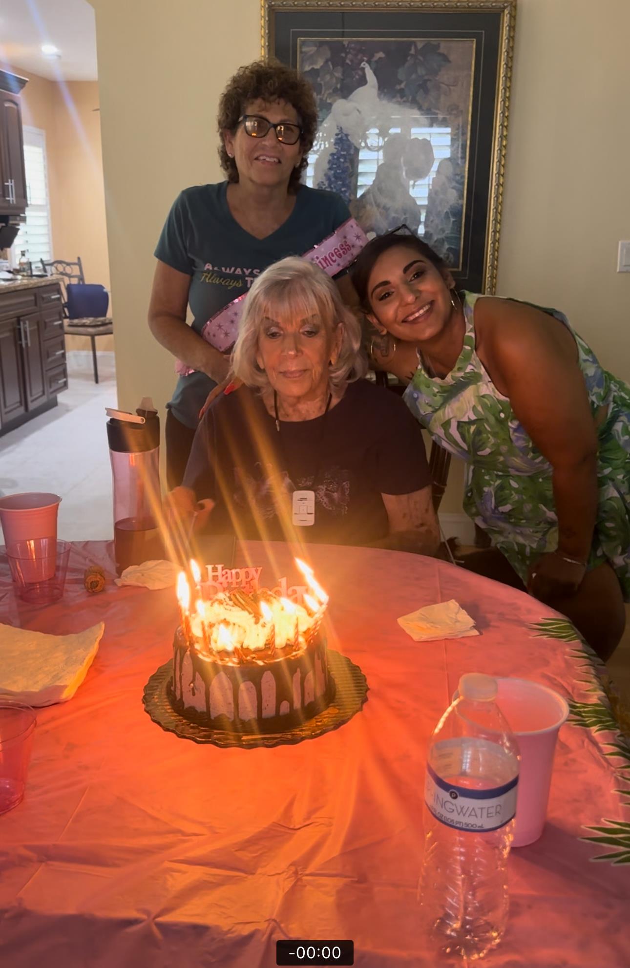 Friends gather around a birthday cake with candles, celebrating a special moment together at home.