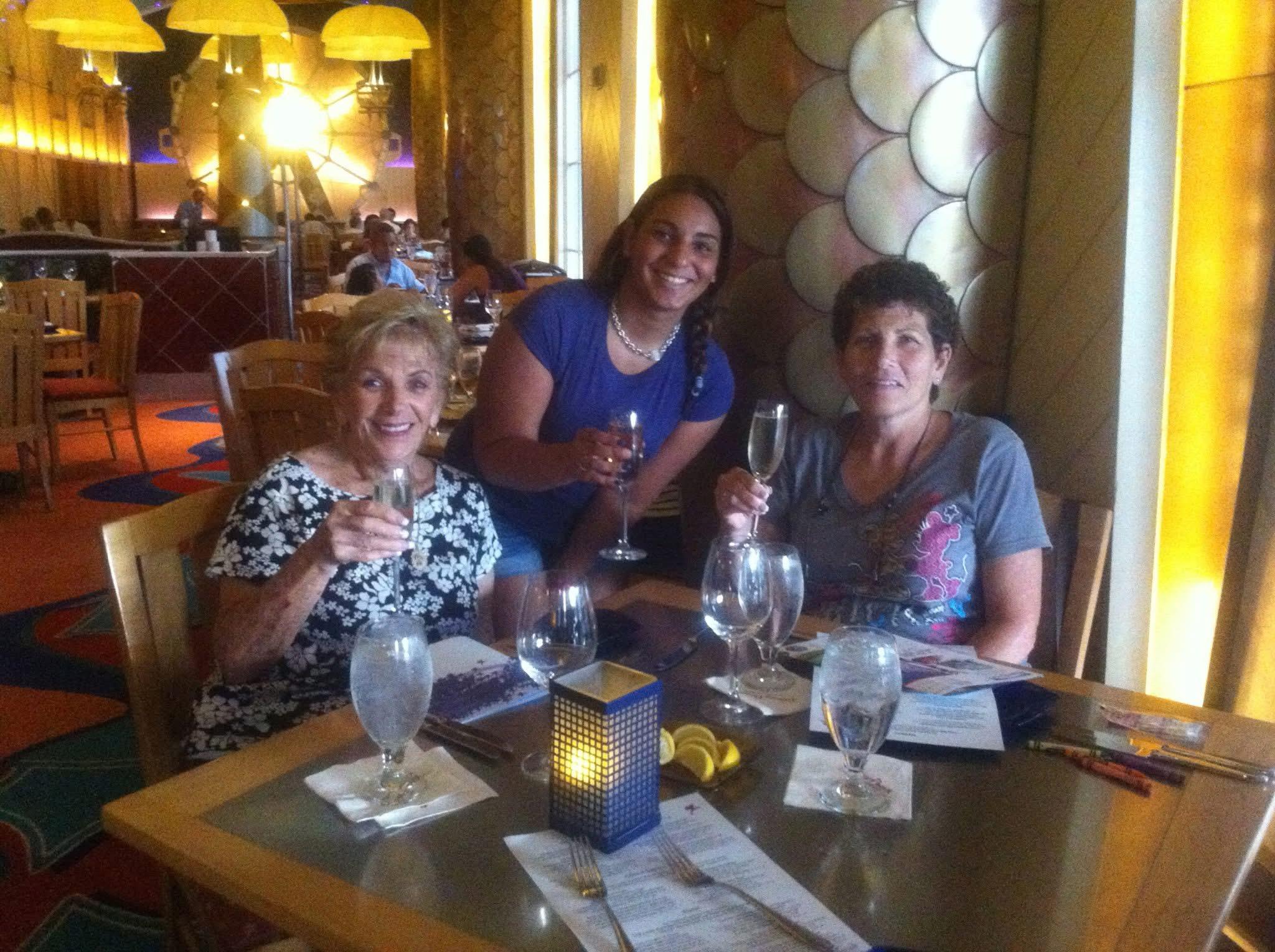Three friends are enjoying drinks and conversation at a restaurant table in the evening.