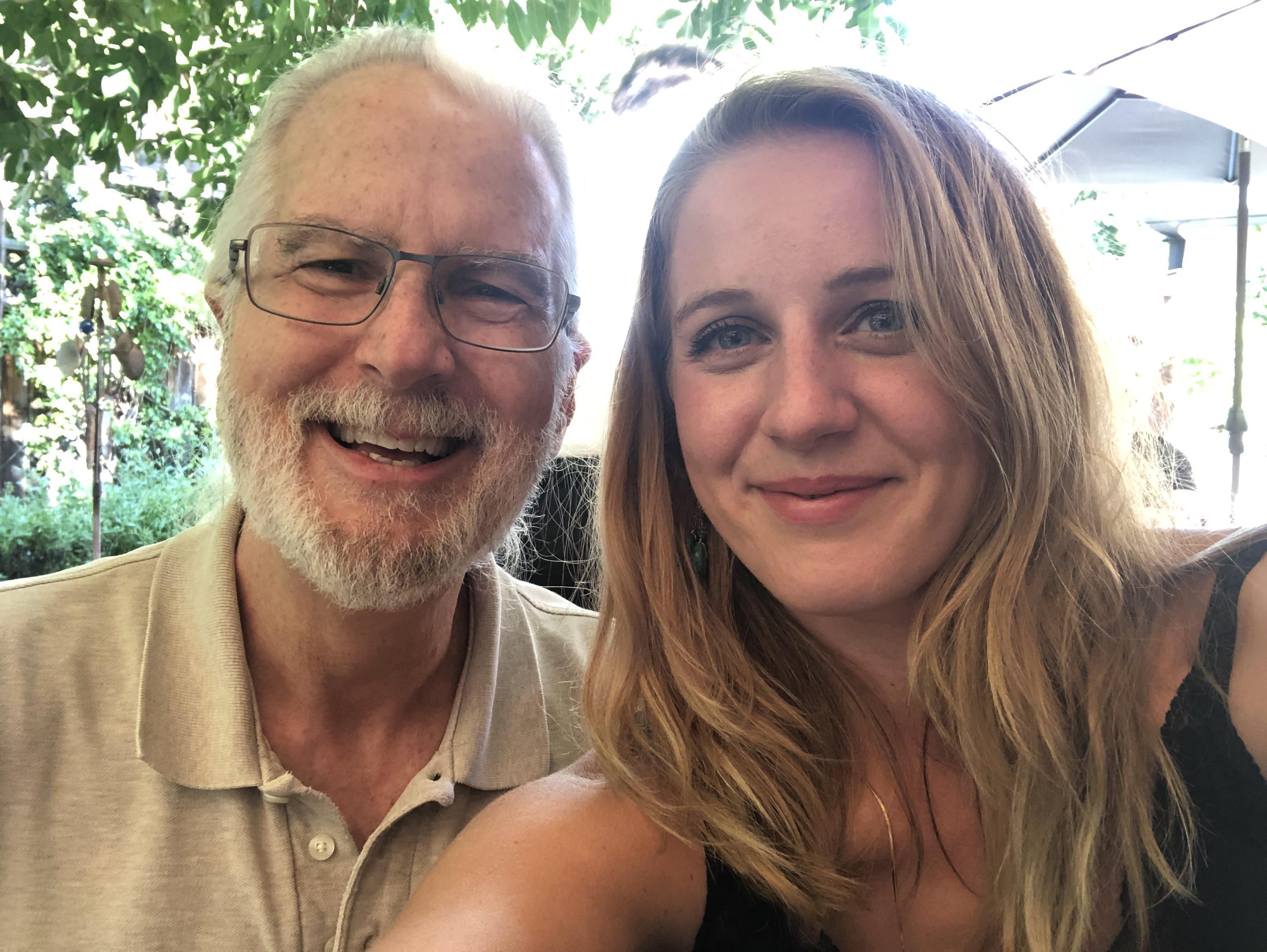 Two individuals take a joyful selfie together while enjoying their time in a garden setting.