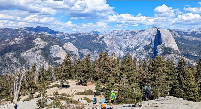 Hikers explore a mountain area with trees and rocky views under a clear sky.