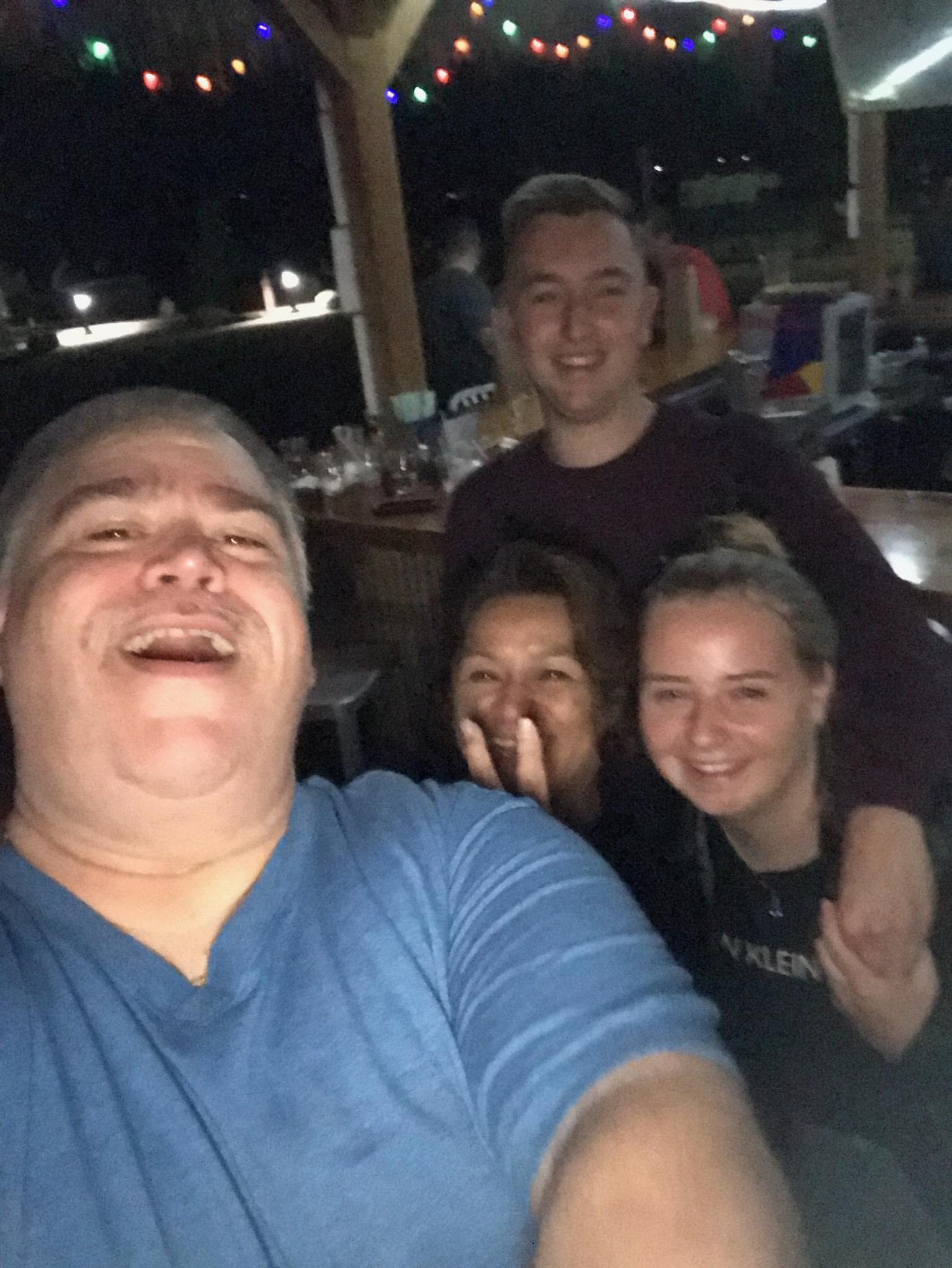 Four friends smile and pose for a group selfie at a social spot after dark.