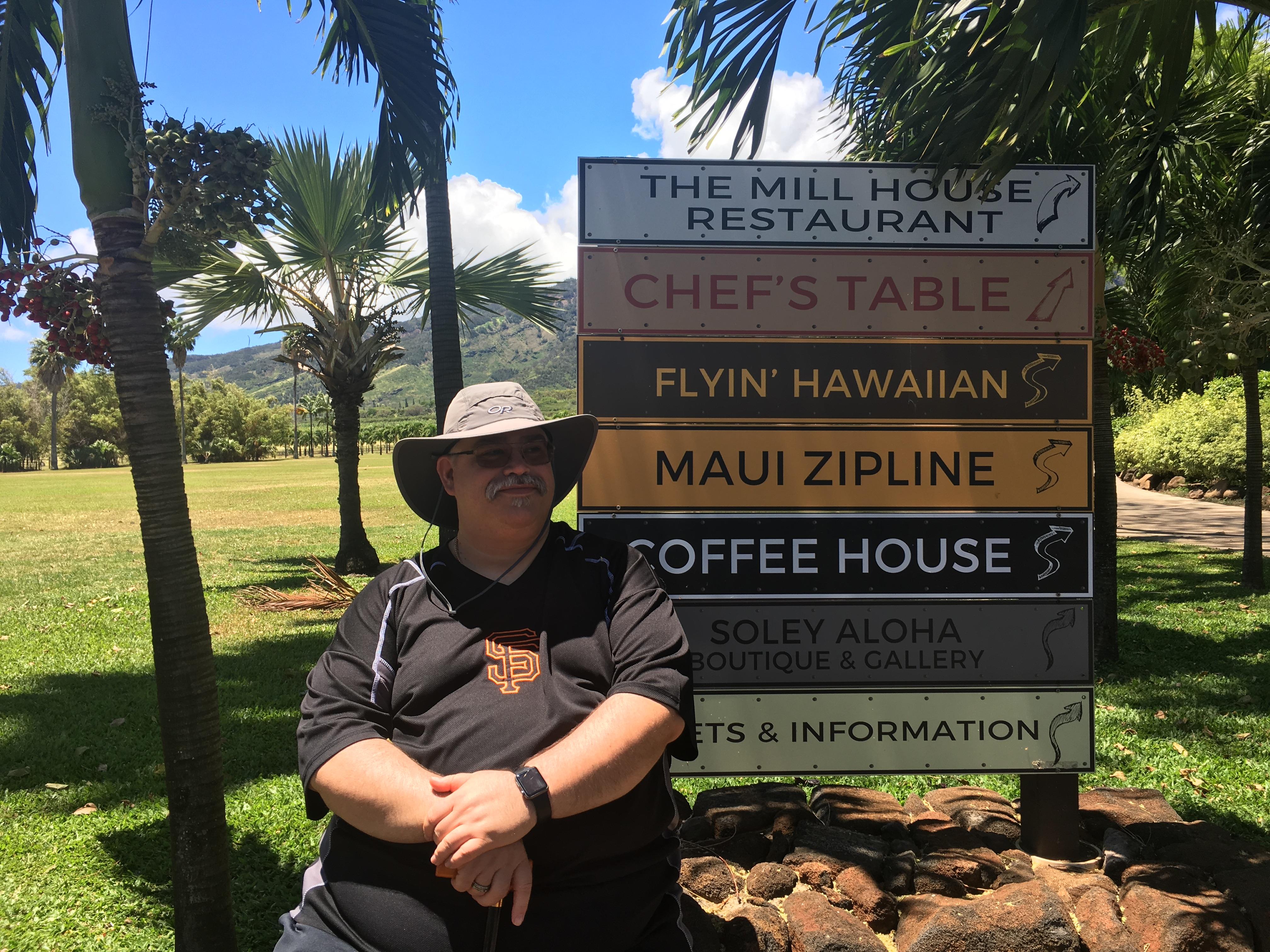 A man rests near the sign for Mill House Restaurant and other spots in Maui during the day.