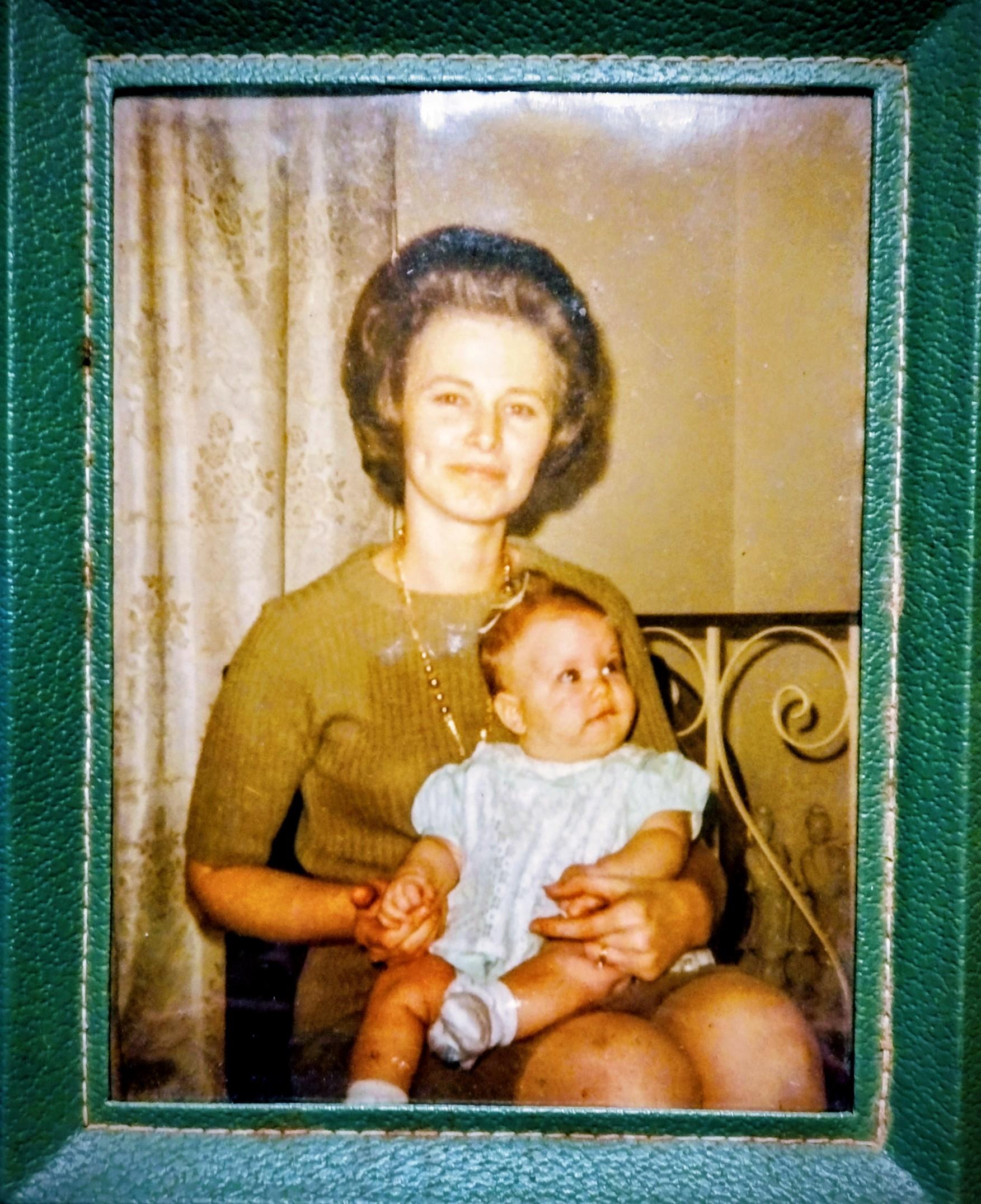 A mother sits in a chair holding her baby in a cozy room with patterned curtains.