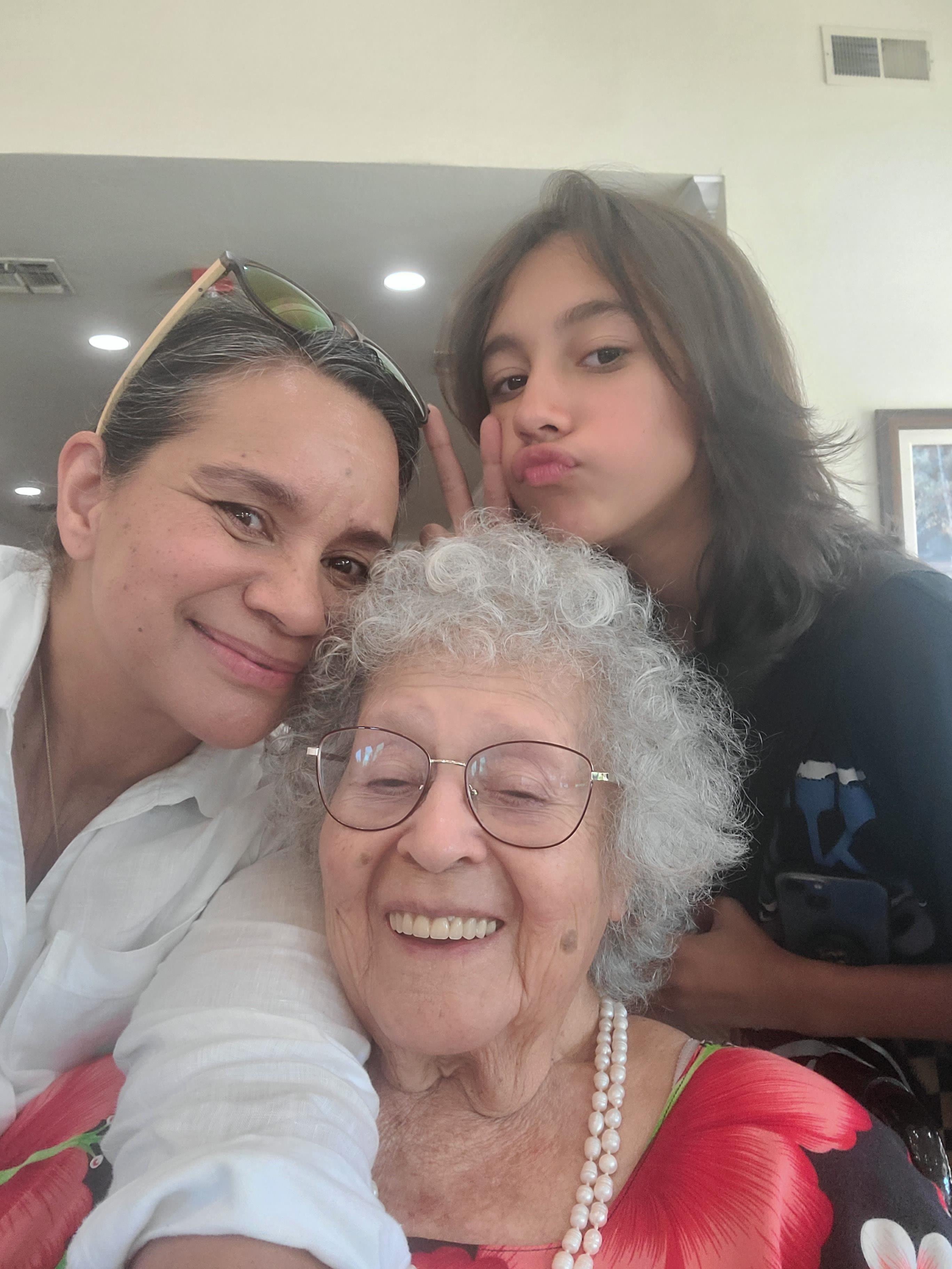 Three family members pose together smiling and enjoying a moment at home during a gathering.