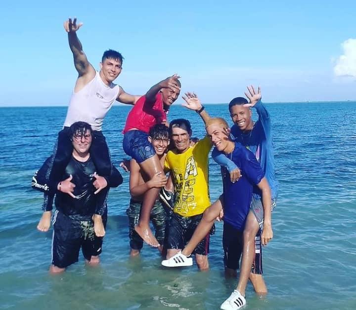 Group of friends play in the water, laughing and taking pictures at the beach on a sunny day.