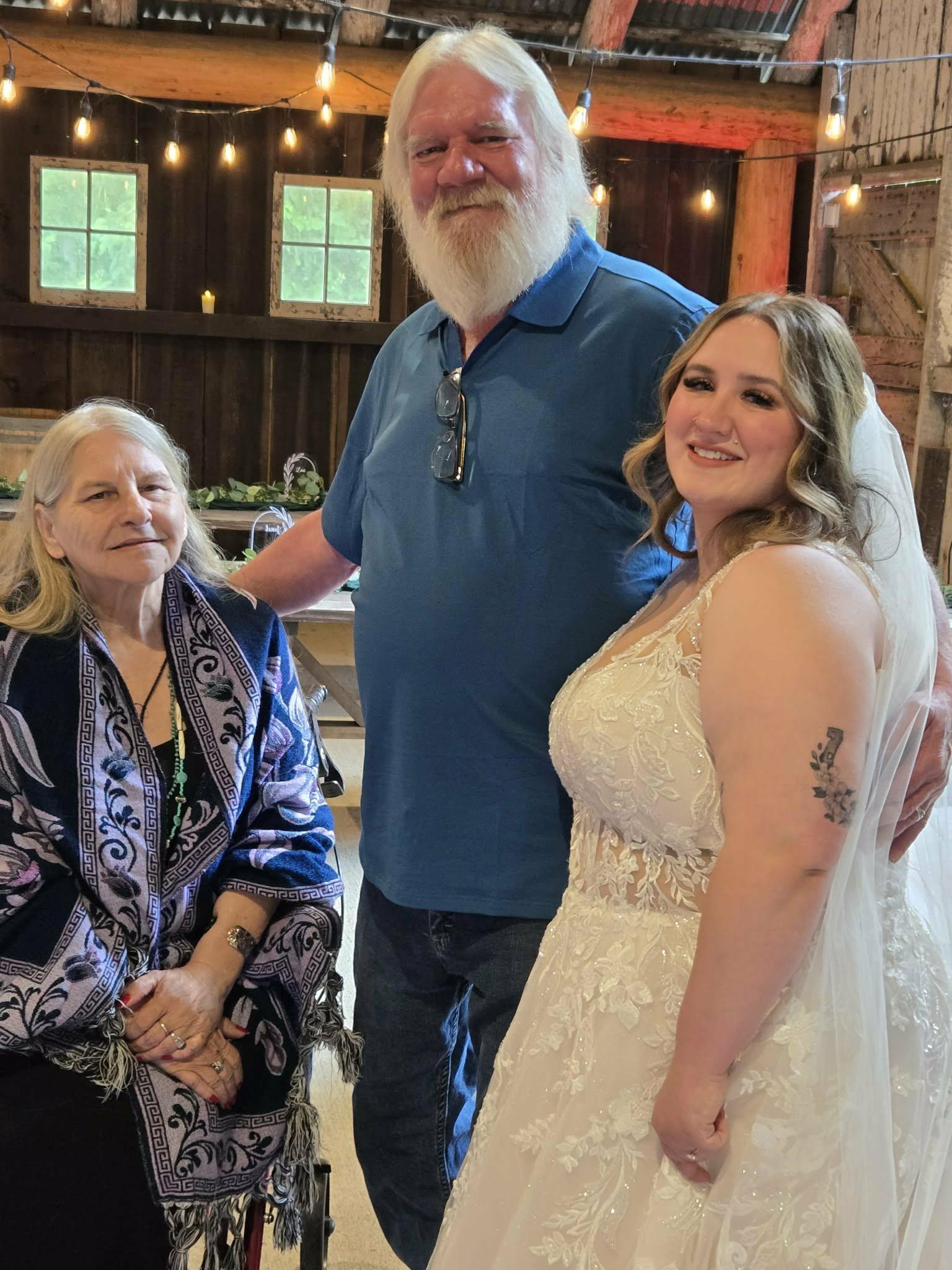 Three relatives pose together at a wedding event in a barn setting with natural light.