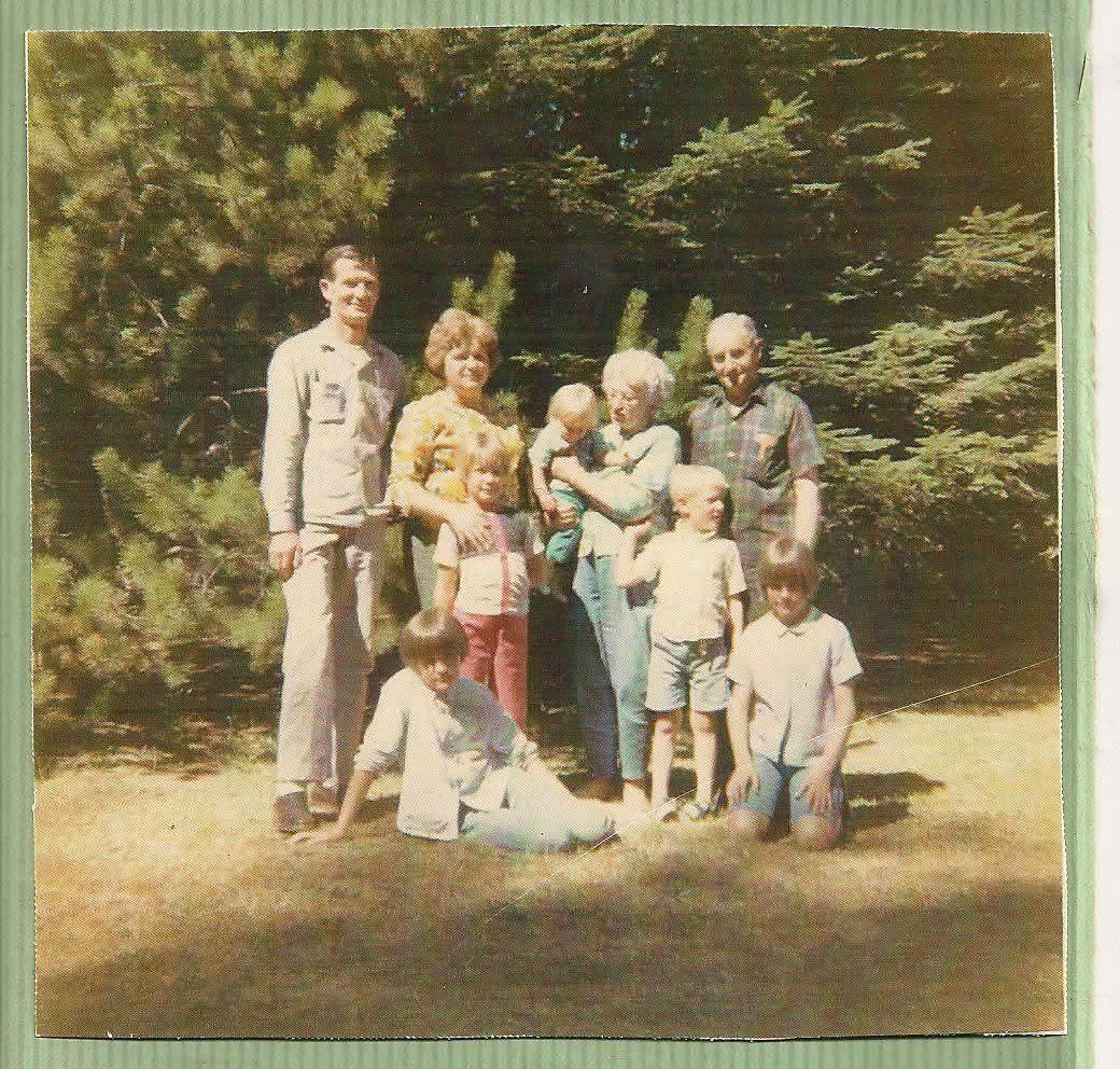 A group of adults and children gather in a park, smiling and posing for a picture.