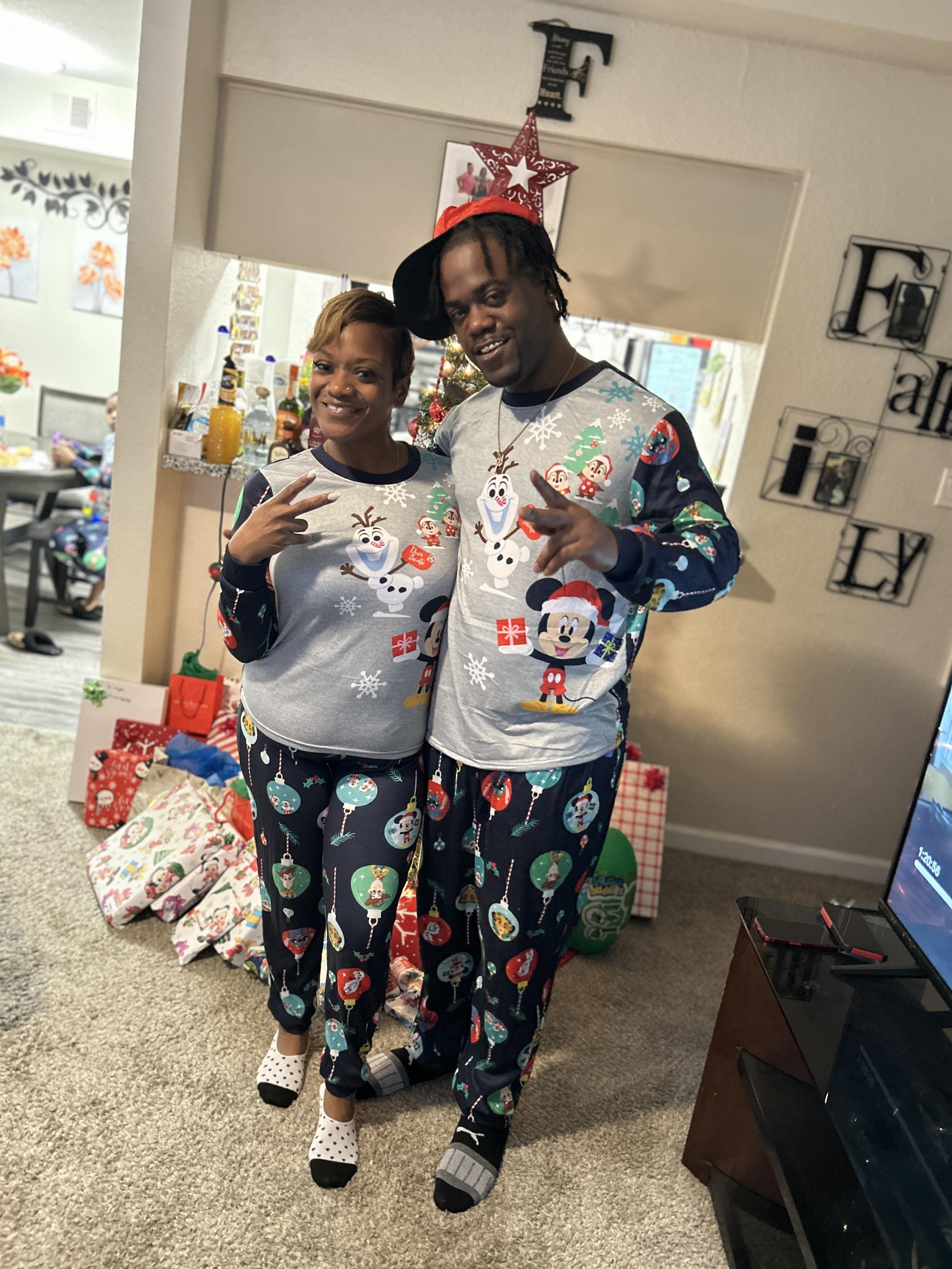 Two people stand together in matching holiday pajamas with decorations around them.