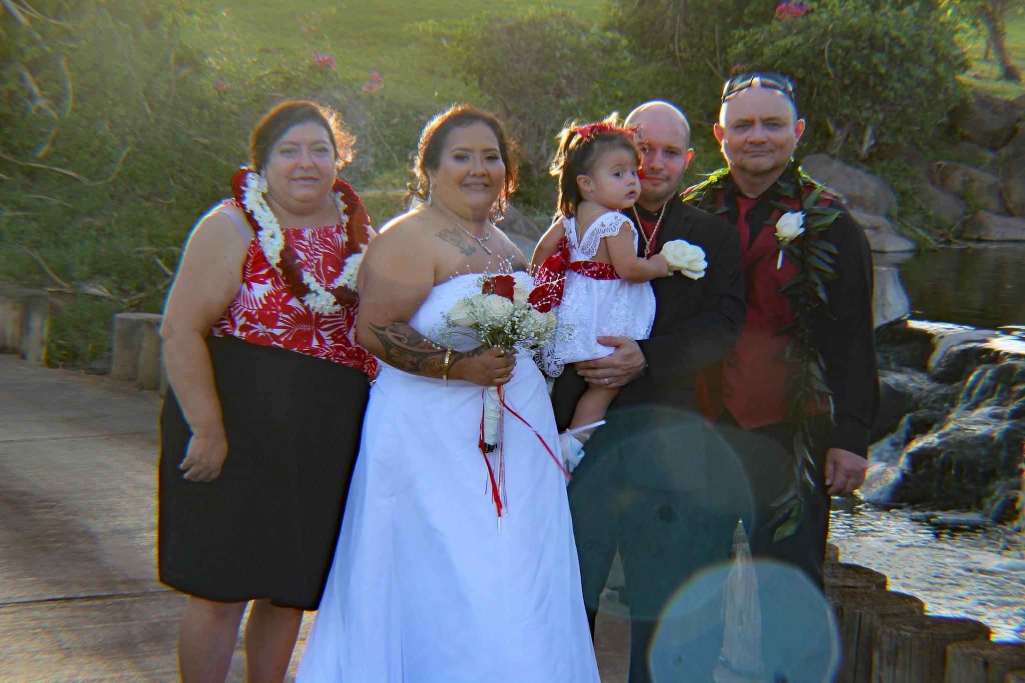 A couple stands with their family after getting married near a garden in Hawaii during sunset.