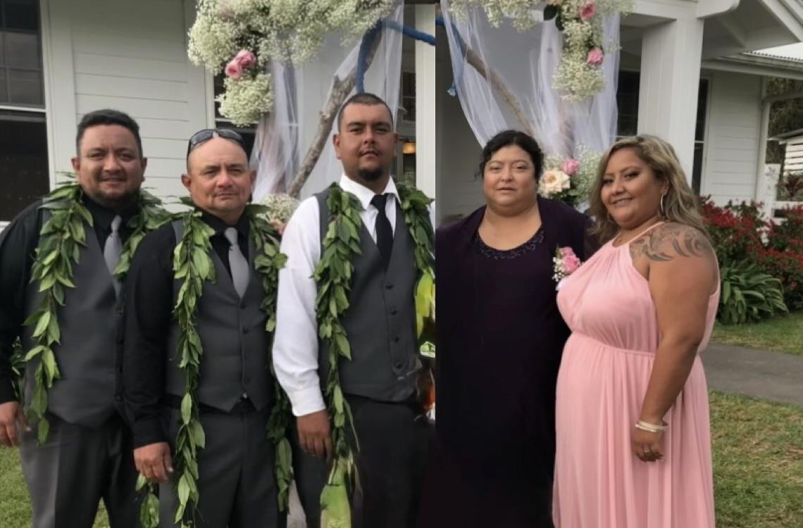 Five people gather for a photo at a wedding. They stand in front of flowers and decorations.