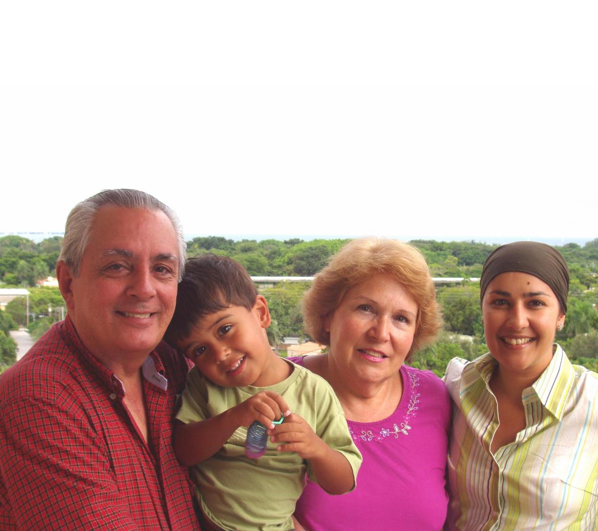 Four family members enjoy time together outdoors with smiles and a child in a green space.