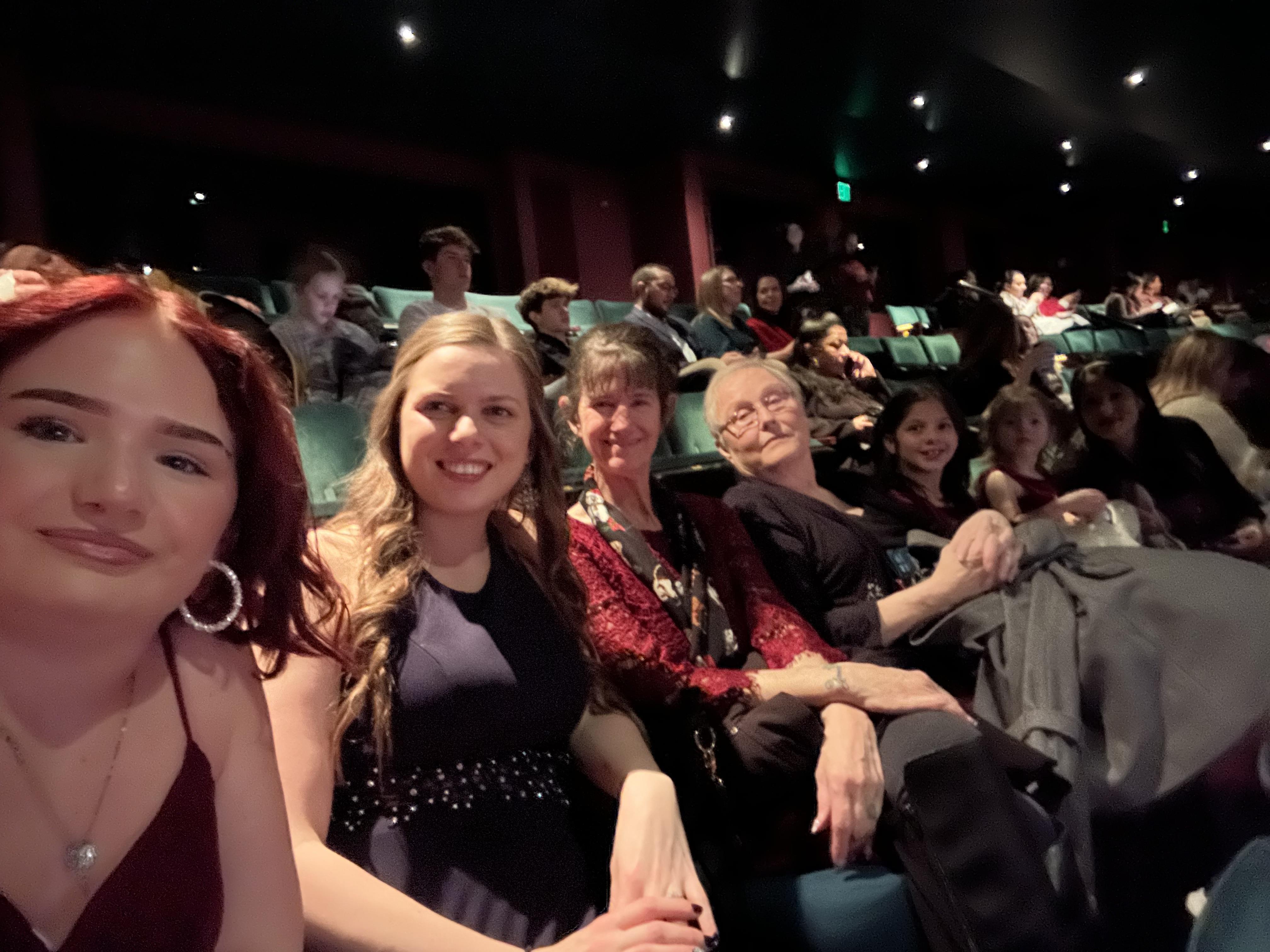 People are sitting together in a theater, waiting for a show to start in a dimly lit setting.