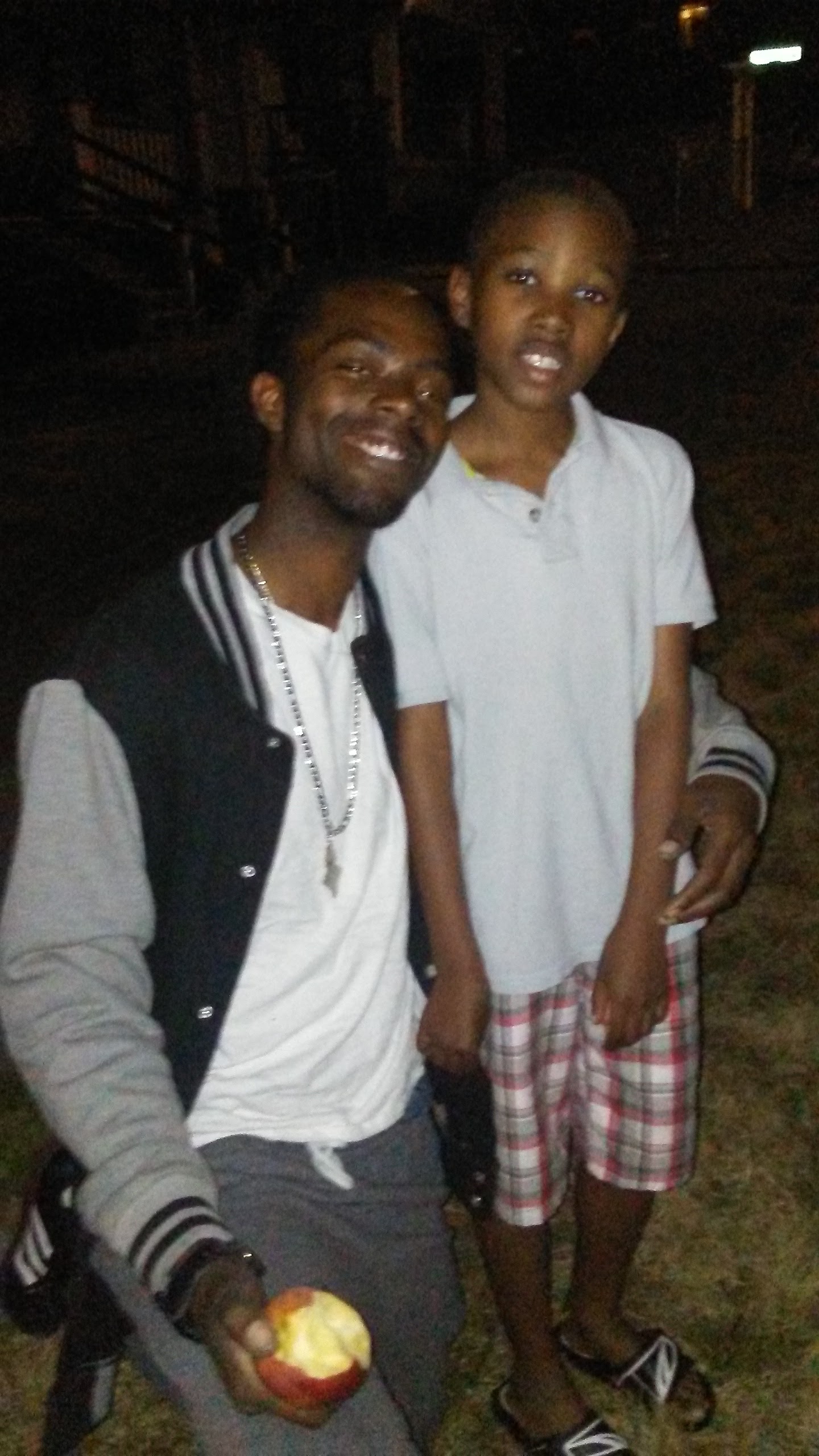 Two individuals stand together smiling while enjoying a night out in a park setting.