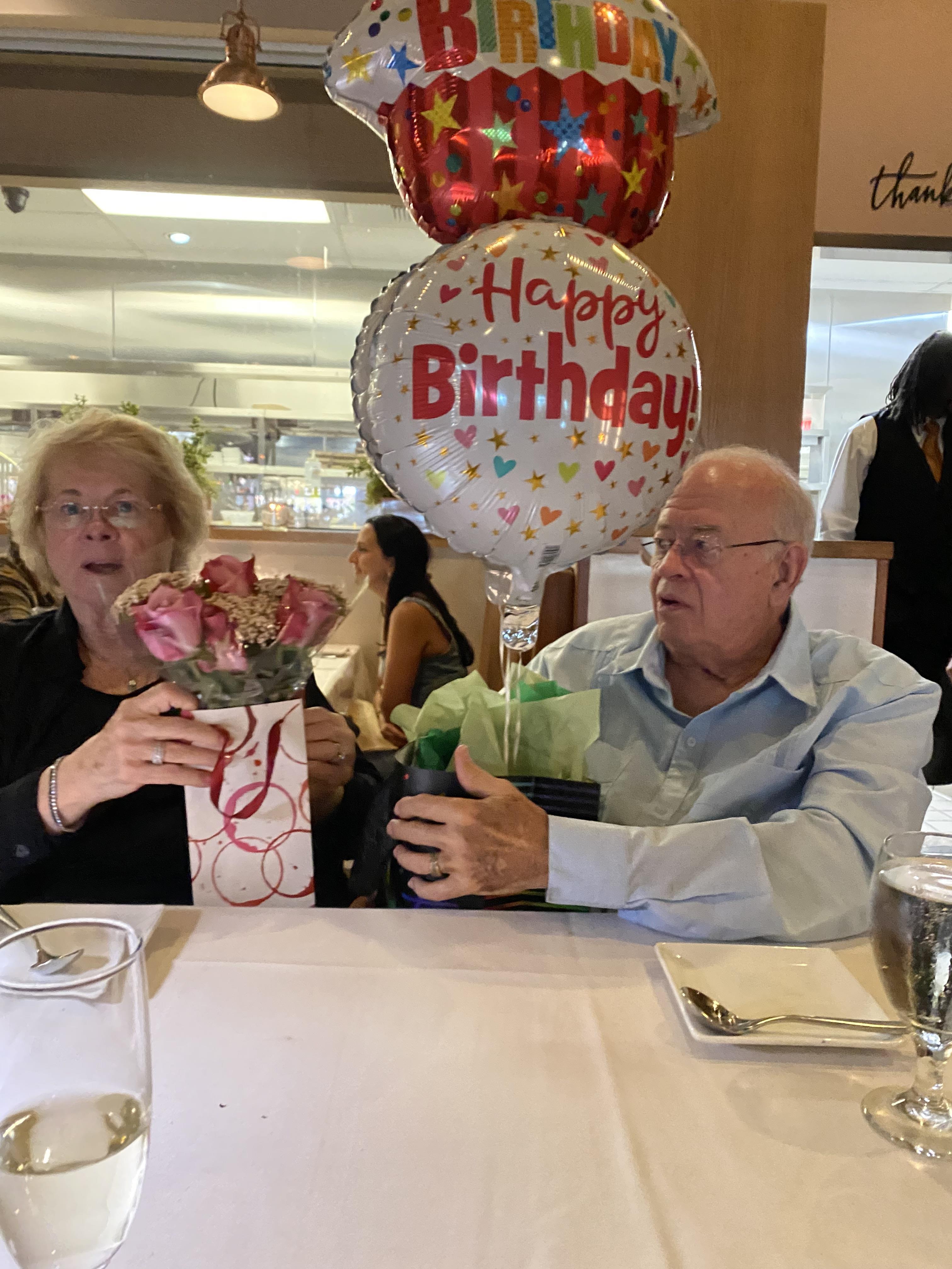 A man and woman sitting at a table with balloons and flowers