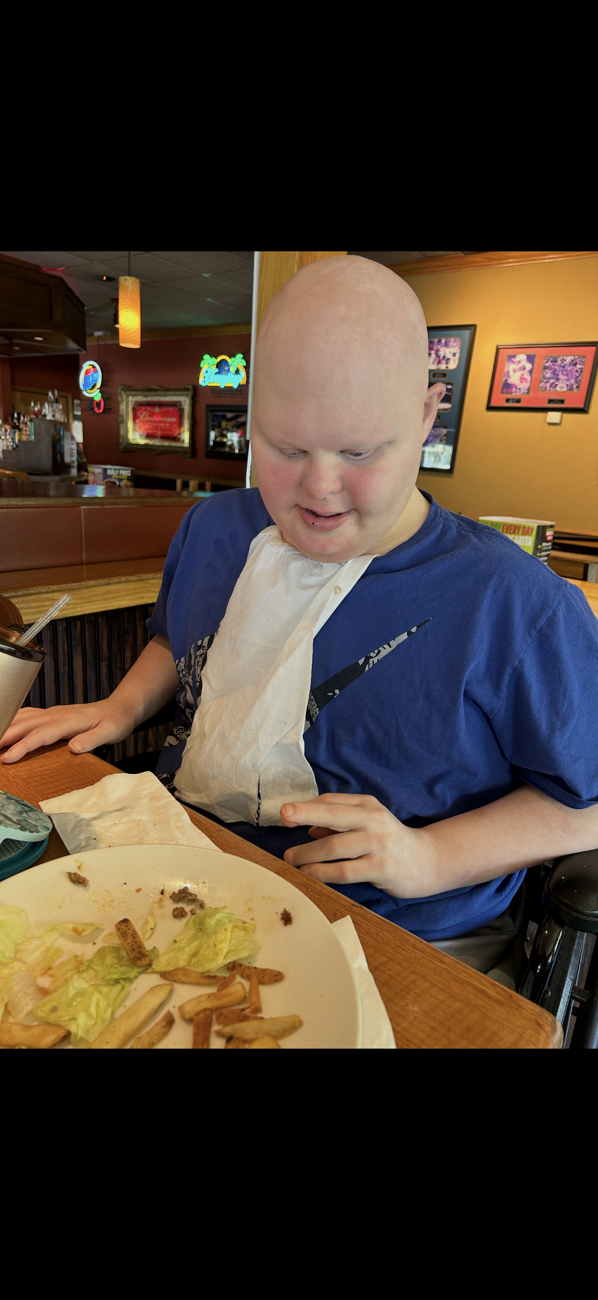 A young boy in a blue shirt enjoys his meal at a restaurant while sitting at a table.